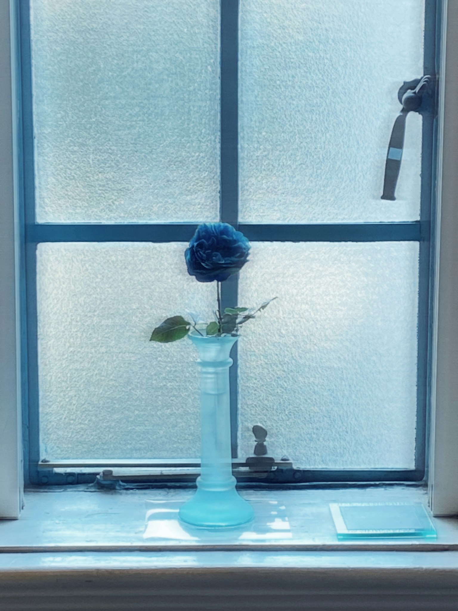 Un jarrón azul con una flor azul en un alféizar