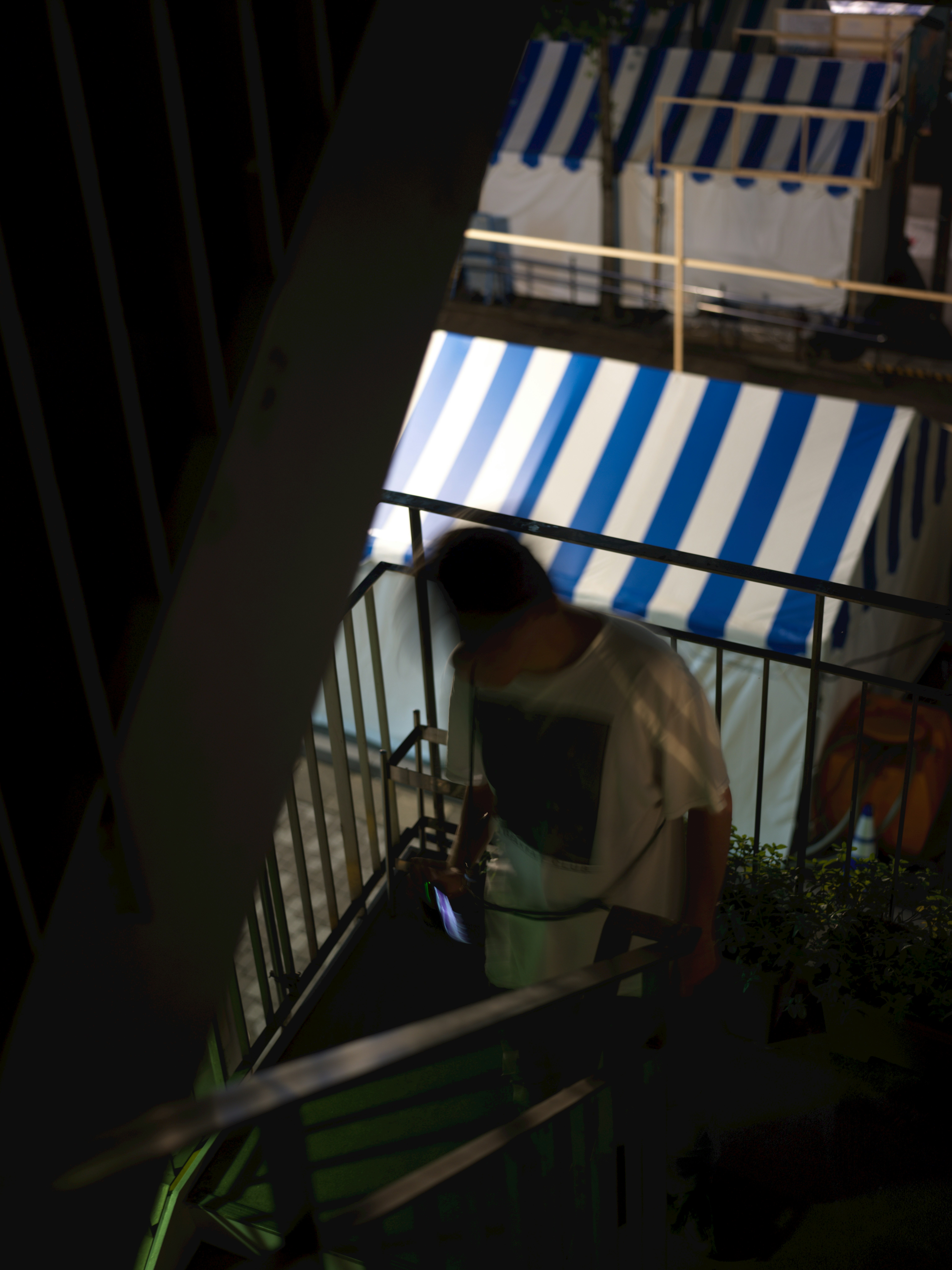 路地の階段で日差しを浴びる人物と青白いストライプのテント画像