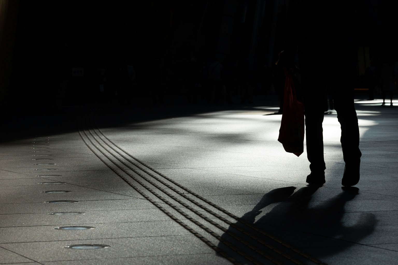 Silueta de una persona caminando con largas sombras en una calle poco iluminada