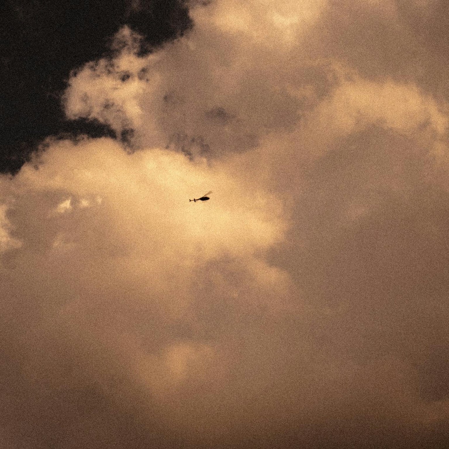 A small aircraft flying between clouds with a dark sky