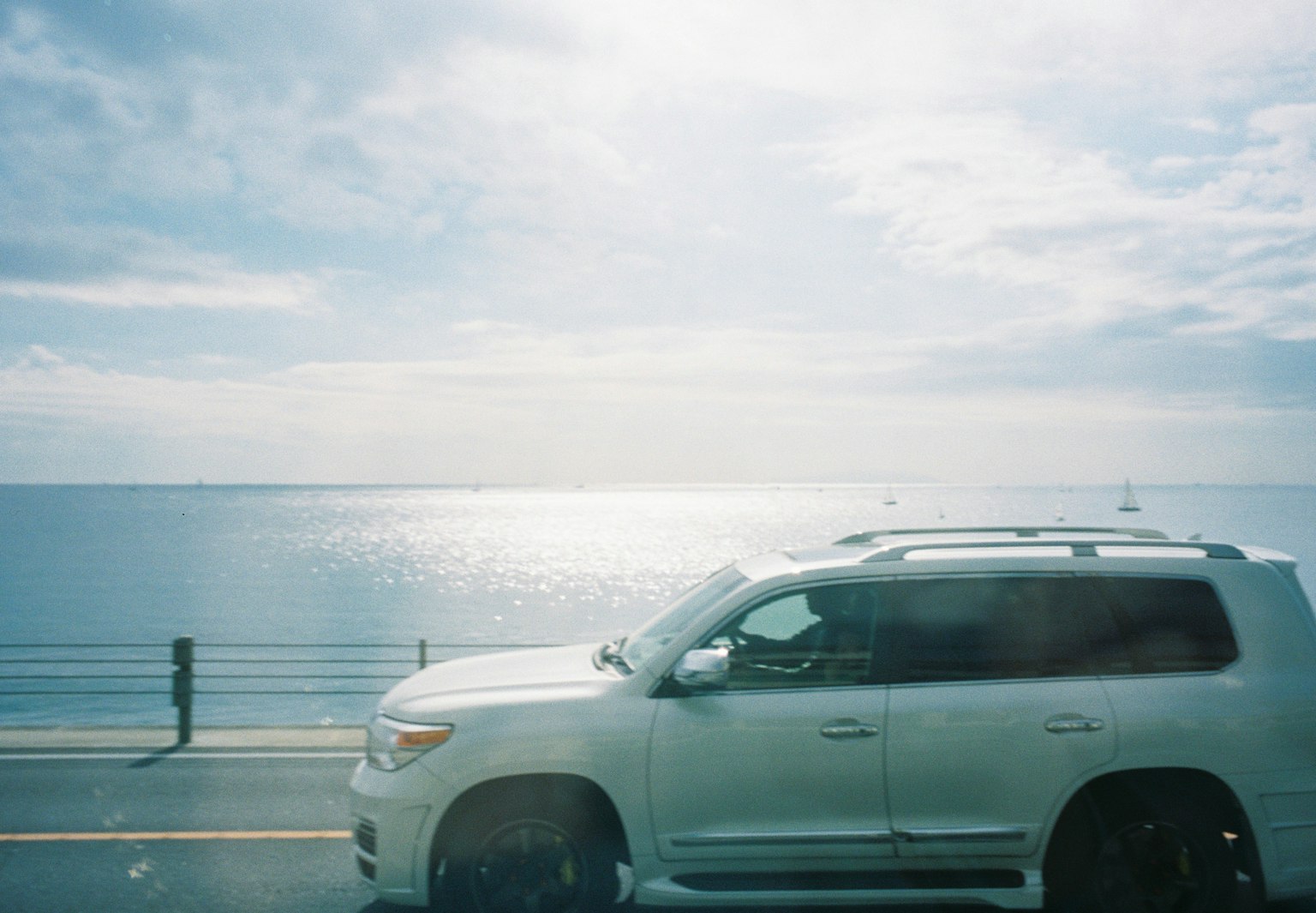 Ein weißer SUV fährt entlang einer Straße mit einem blauen Ozean und einem hellen Himmel im Hintergrund