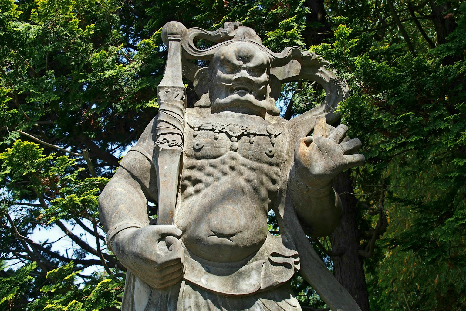 Large stone statue of a guardian deity holding a staff with a fierce expression