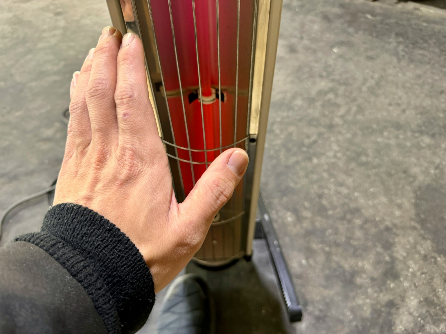 Una mano tocando un dispositivo de calefacción con elementos rojos