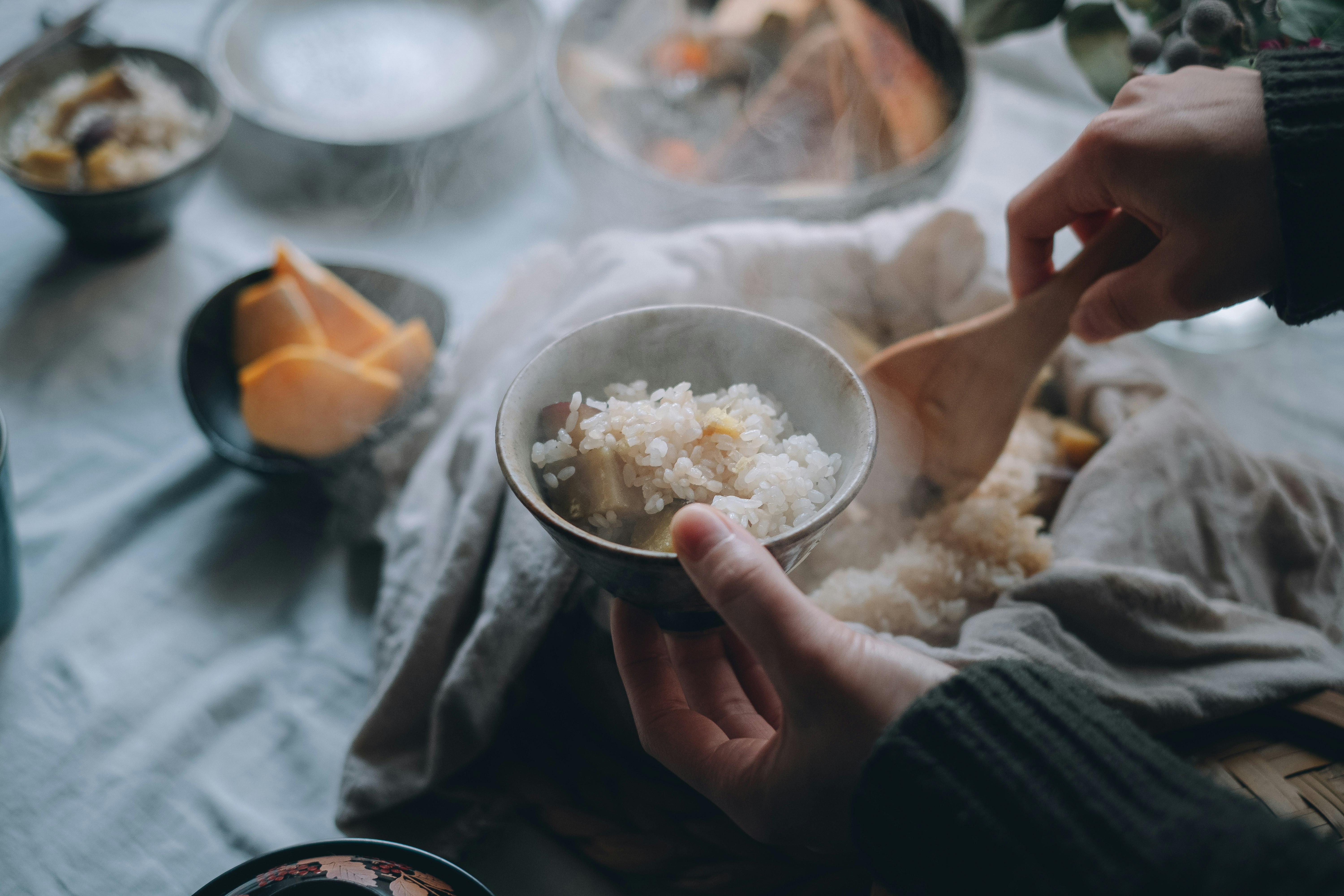 手に持った小鉢の塩味の具材と食卓の料理