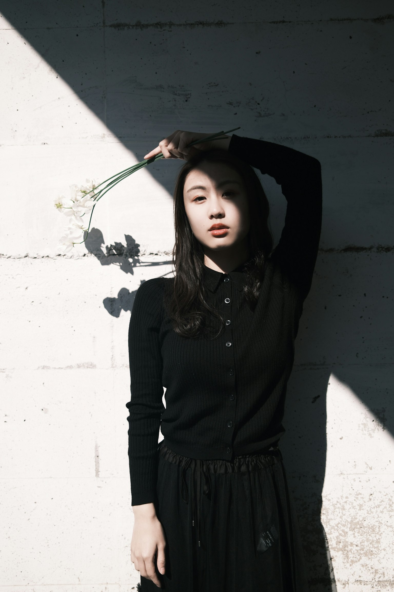 黒い服を着た女性が壁に寄りかかり花を持っている