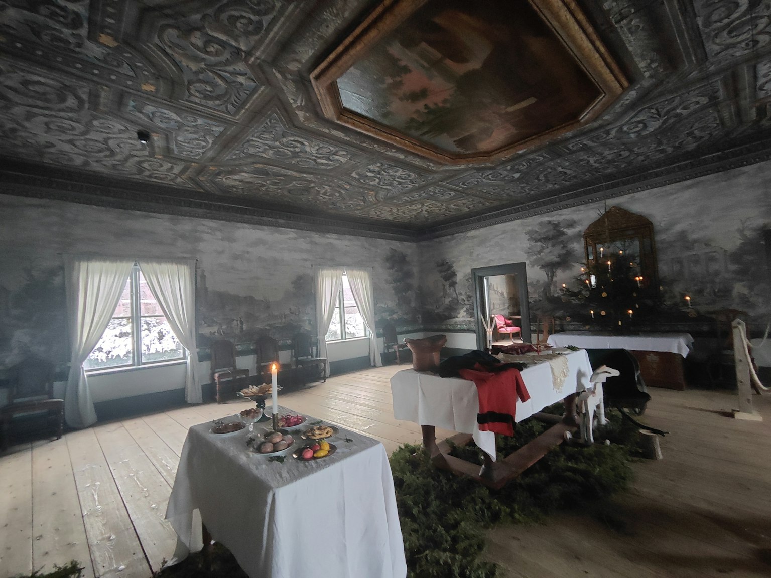 Vista interior de una habitación con techo decorativo y velas mesa adornada con frutas y follaje