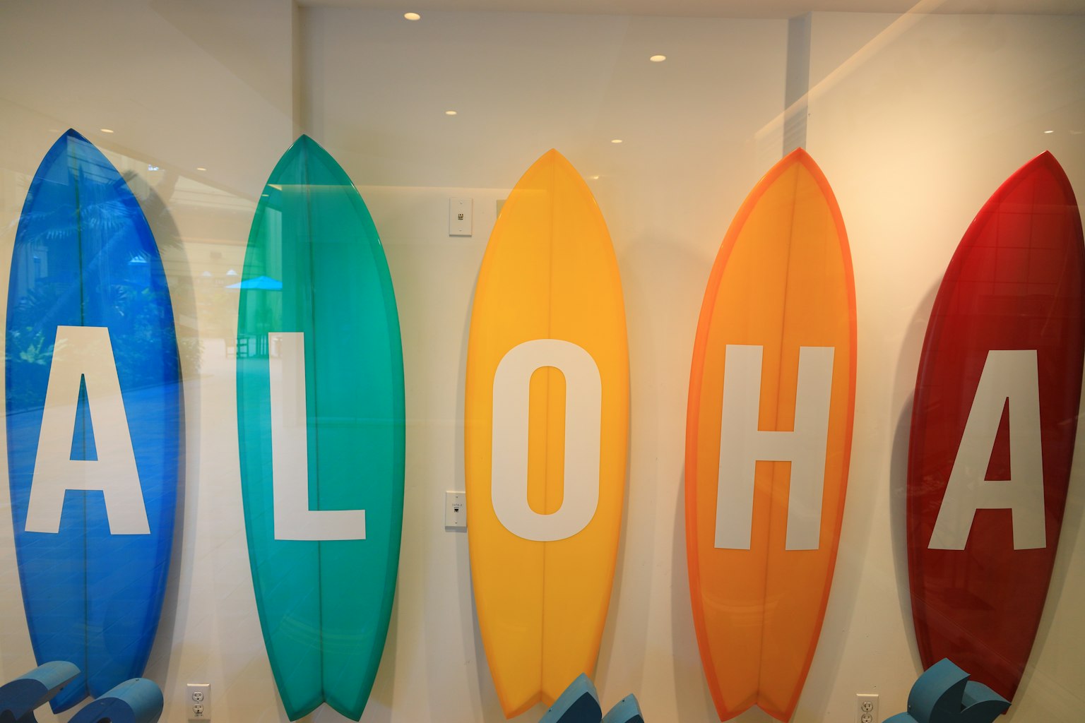 Des planches de surf colorées en bleu, vert, jaune, orange et rouge affichant le mot ALOHA en lettres blanches