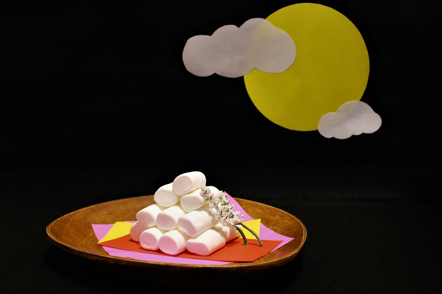 A mound of marshmallows on a plate with a yellow sun and white clouds in the background