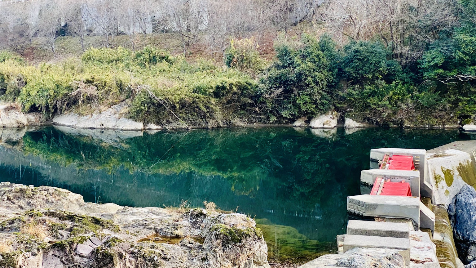 Pemandangan sungai yang tenang dengan tangga batu merah dan vegetasi hijau subur di sekitarnya
