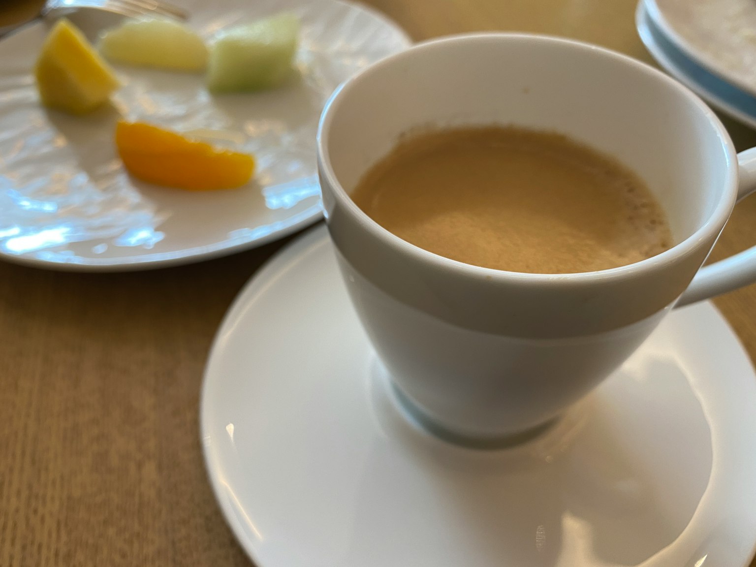 Weißer Kaffeebecher mit einem kleinen Teller gemischter Früchte