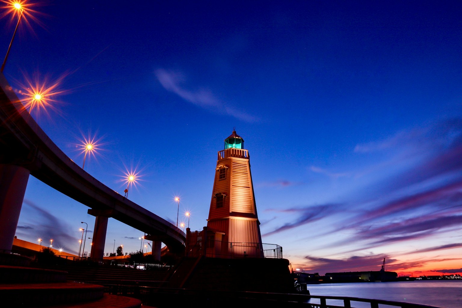 Faro illuminato al crepuscolo con un ponte sopra