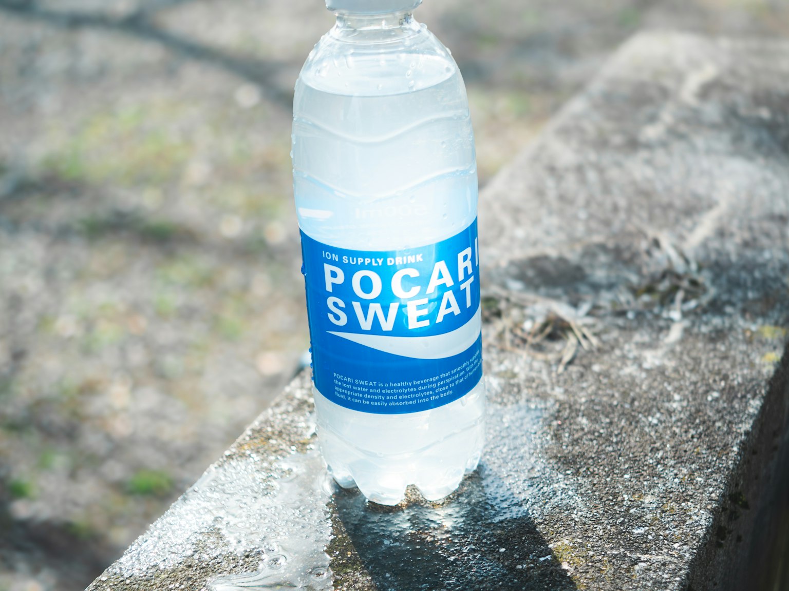Một chai nước đặt trên bê tông có nhãn màu xanh Pocari Sweat