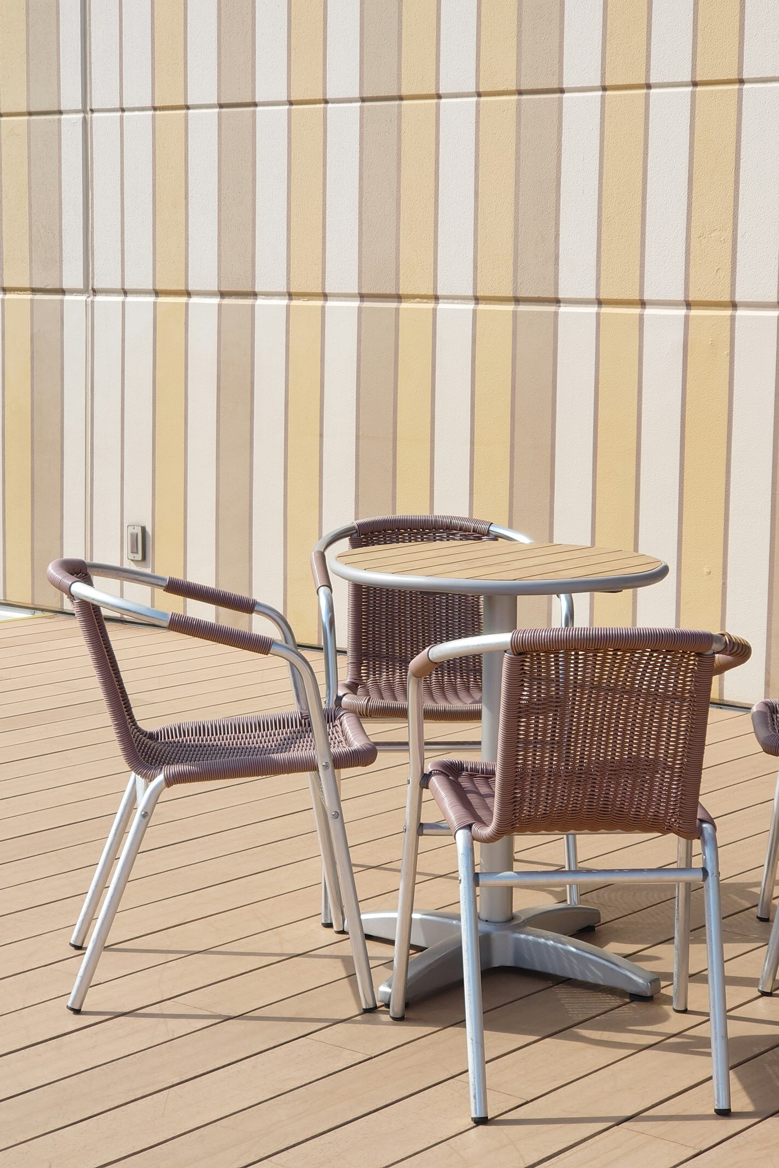 Ein runder Tisch mit zwei Stühlen auf einer Terrasse vor einer gestreiften Wand
