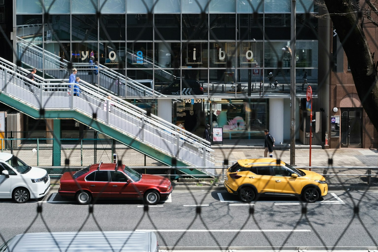 Scena di strada con un'auto rossa e un'auto gialla parcheggiate scale e negozio visibili