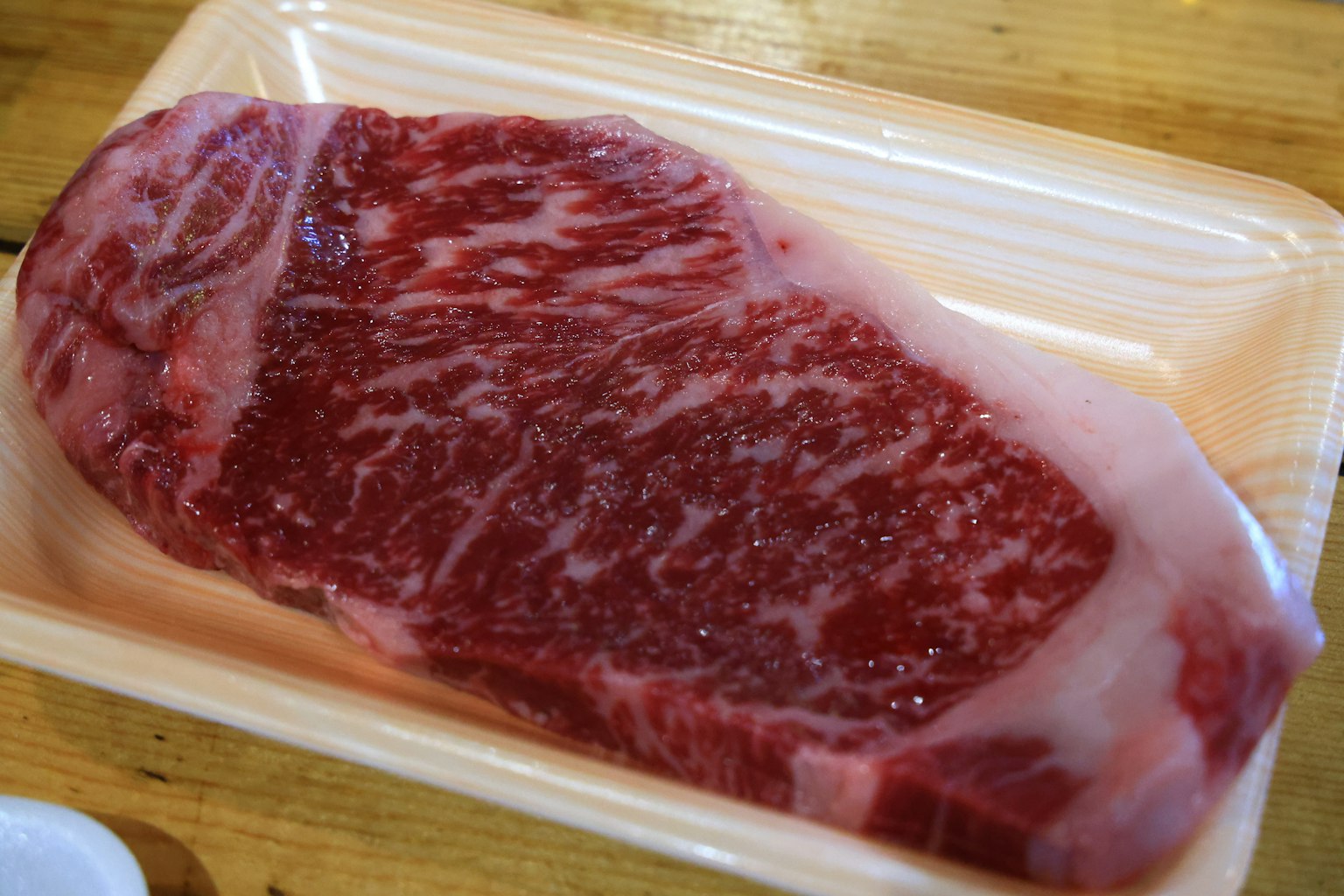Bistec de res crudo con textura marmoleada en una bandeja blanca