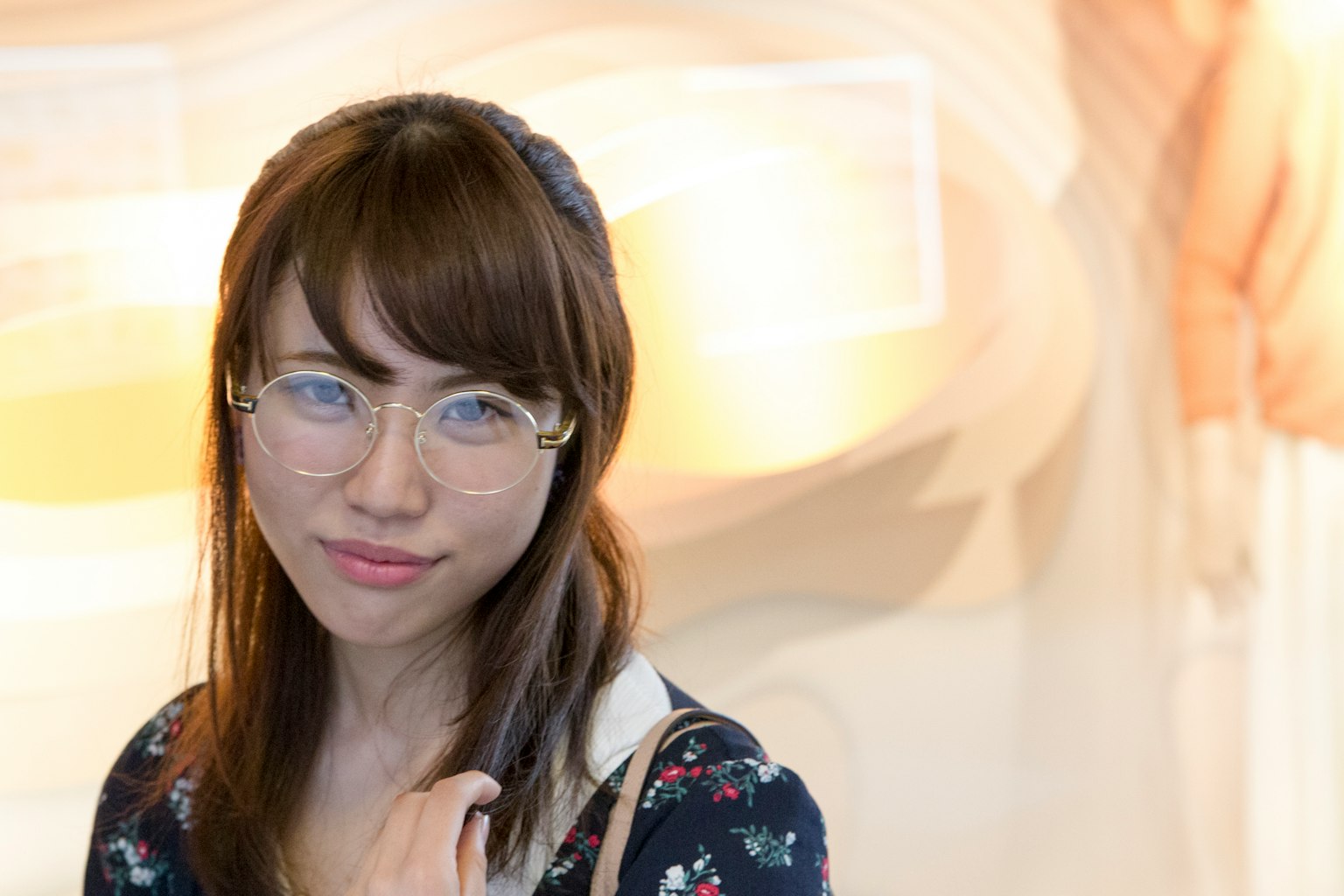Một người phụ nữ đeo kính mỉm cười với phông nền màu mềm mại