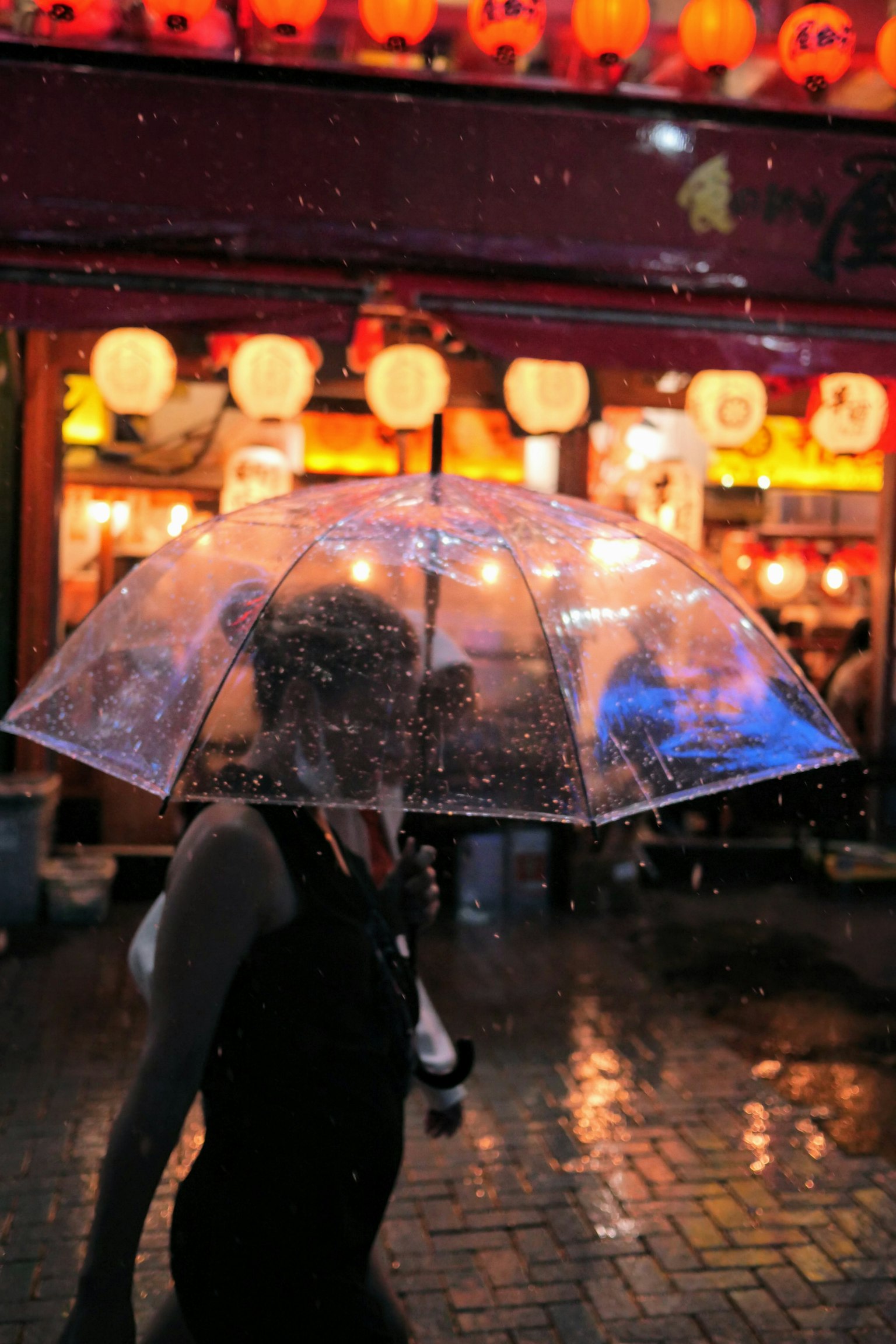 手持透明雨伞的女性在雨中行走背景有明亮的灯笼照亮