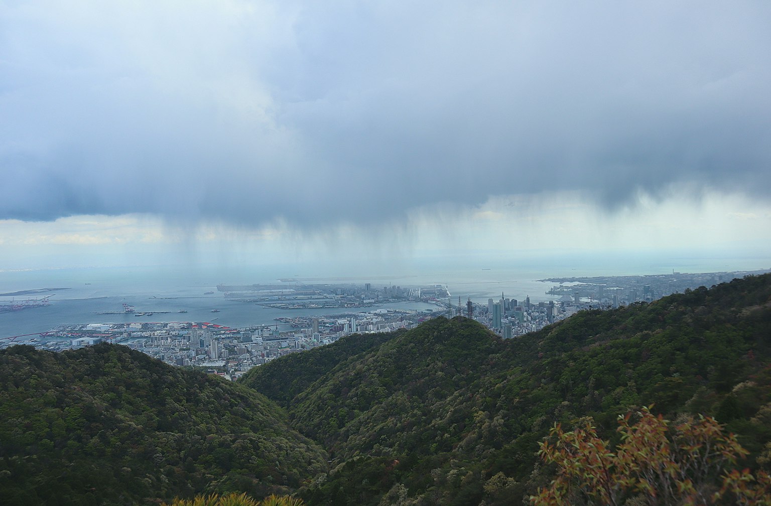 View from a mountain showing a city and ocean under cloudy skies