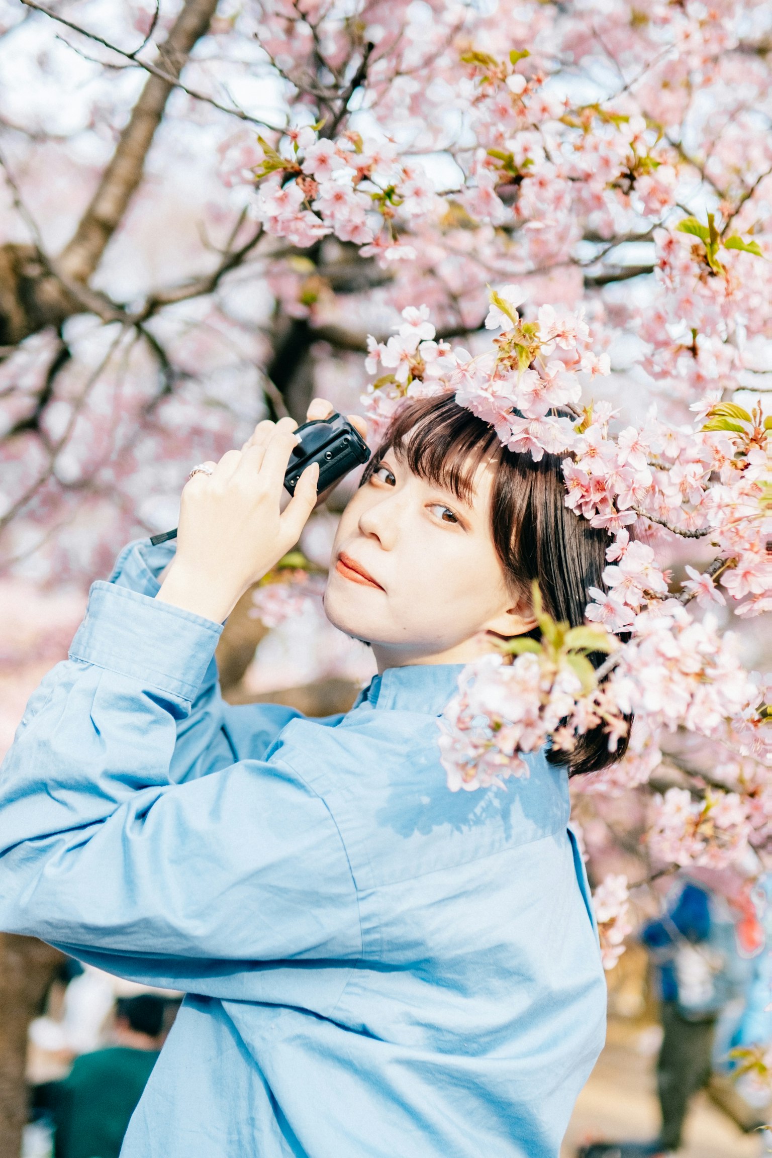 Donna che tiene una macchina fotografica circondata da fiori di ciliegio