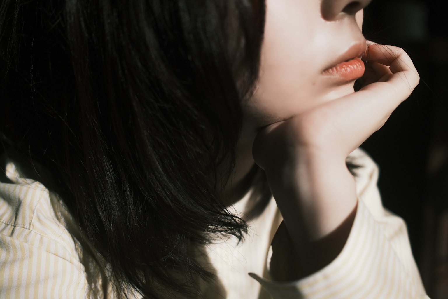 女性の横顔が映る写真 髪は黒くて長い 口元は控えめな色合いで手が顎に添えられている