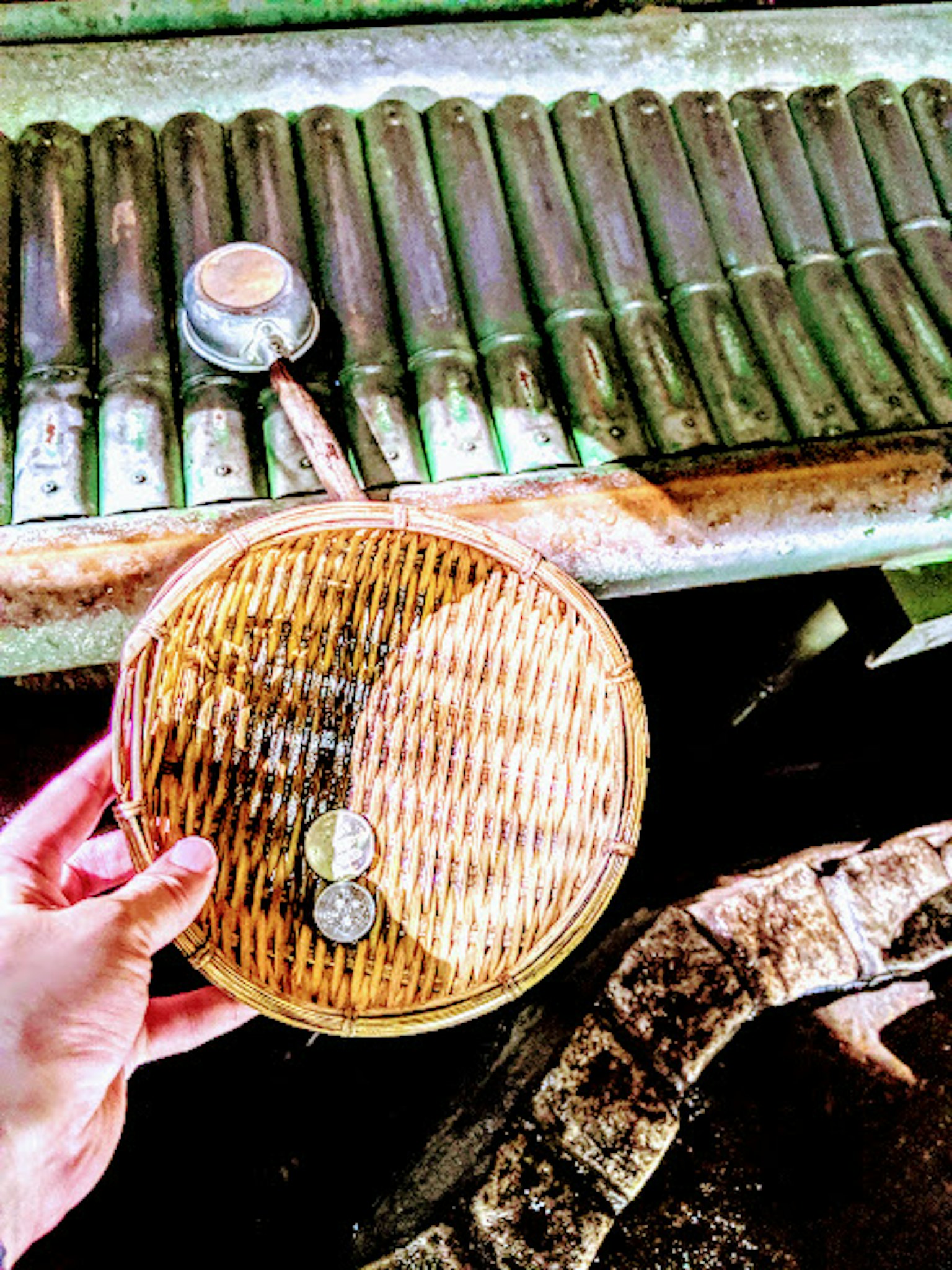 Hình ảnh một bàn tay cầm giỏ tre với những đồng xu trên bề mặt gỗ