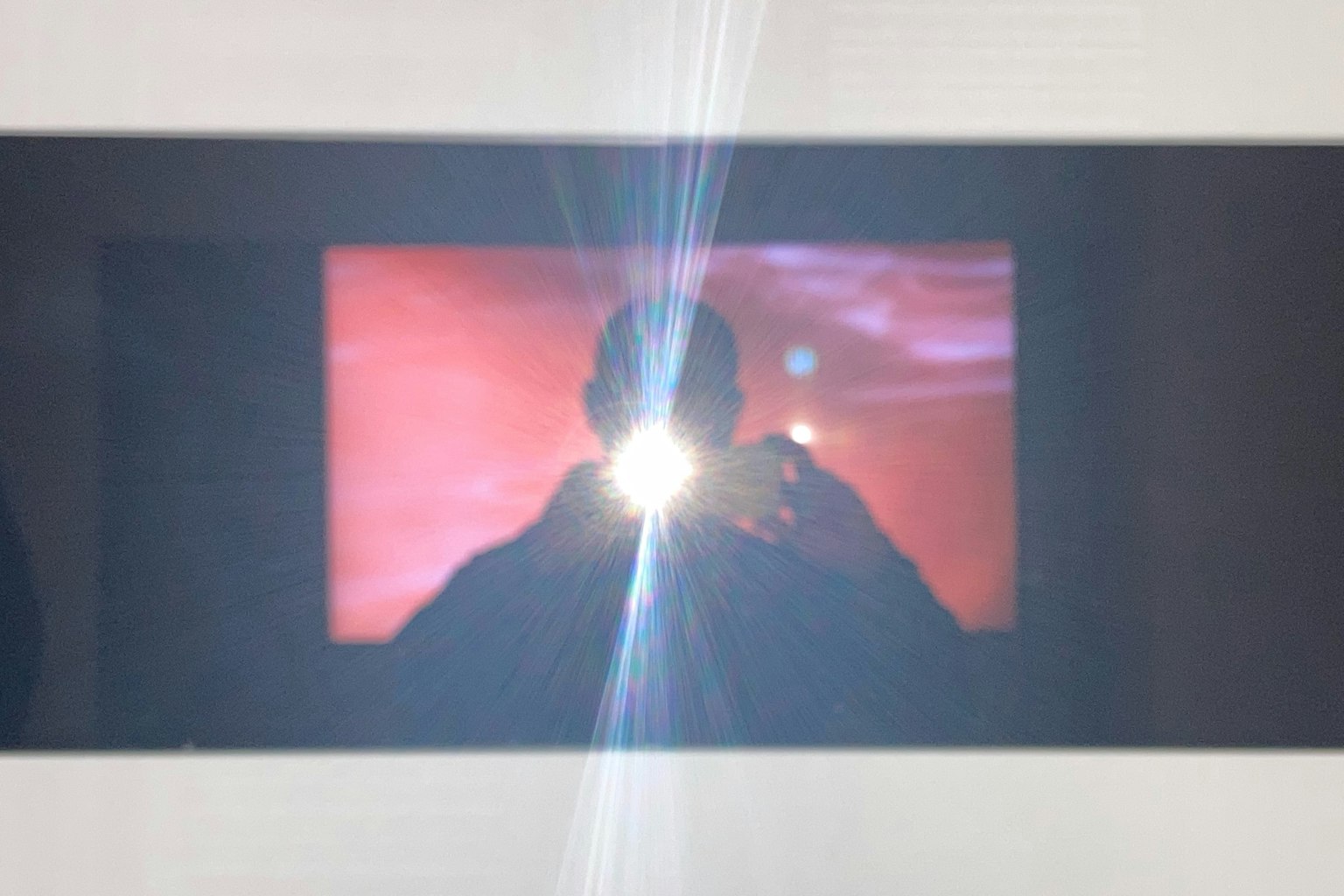 Silhouette einer Person, beleuchtet durch den Kamerablitz, mit abstrakten roten Lichtmustern im Hintergrund