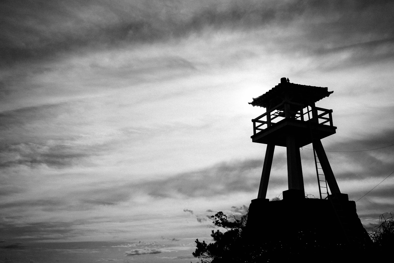 Silhouette di una torre di avvistamento contro un cielo nuvoloso in bianco e nero
