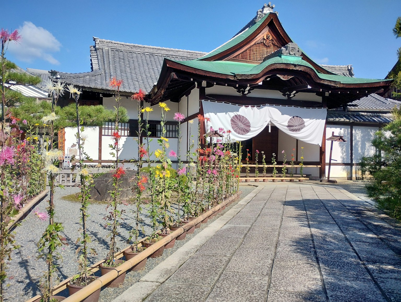Traditional Japanese temple exterior with green roof and white curtain surrounded by blooming flowers