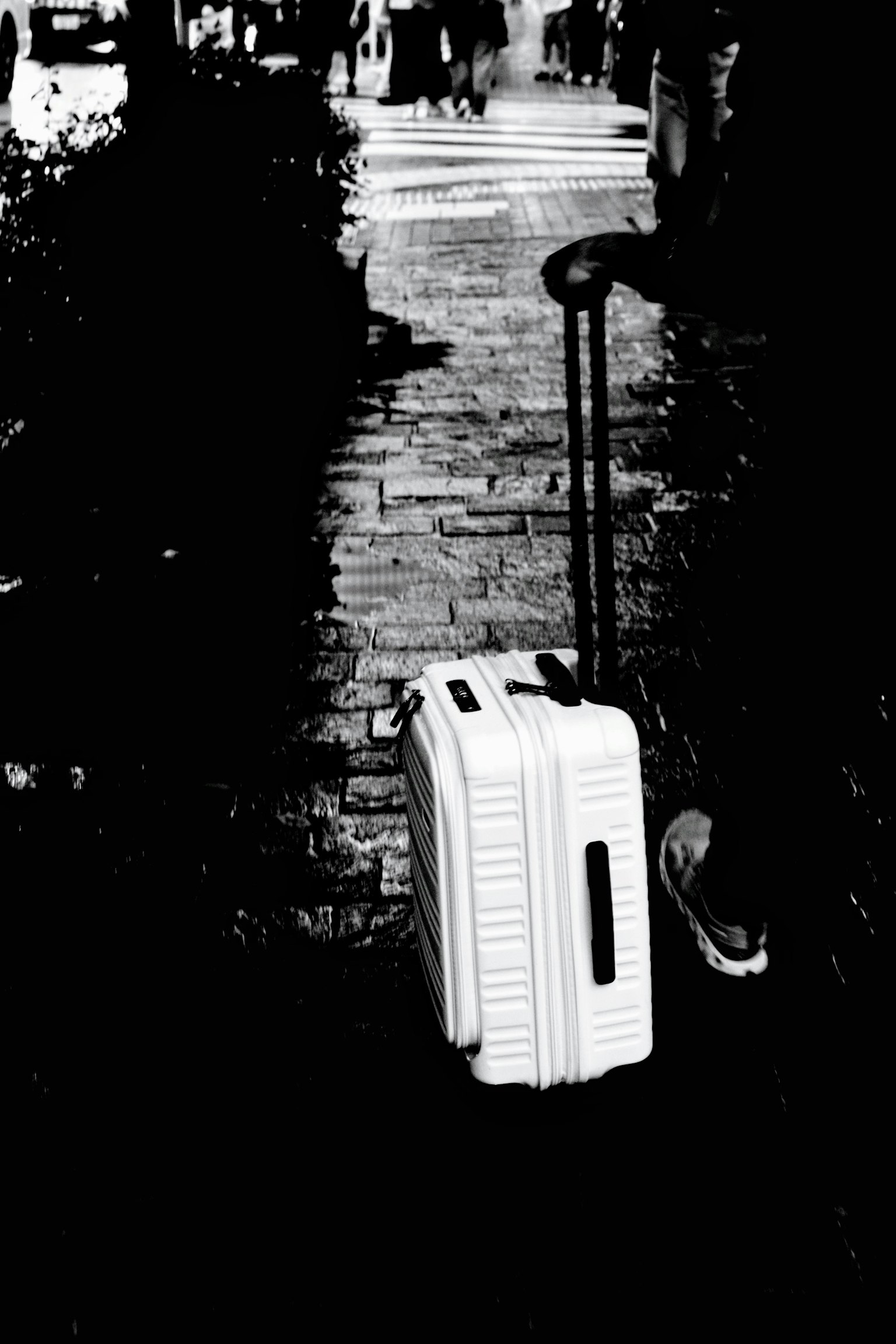 A white suitcase left on a city sidewalk in black and white