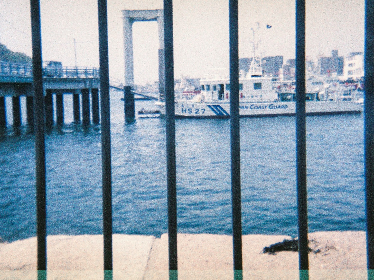 Blick auf einen Hafen durch einen Zaun mit einem Boot und blauer Wasser