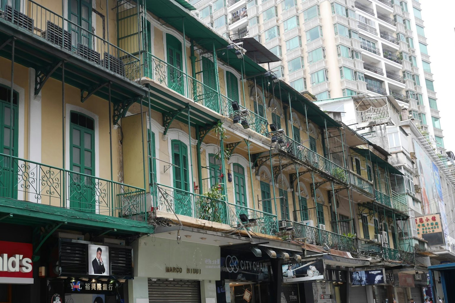 Façade d'un ancien bâtiment avec balcons verts et un gratte-ciel moderne en arrière-plan