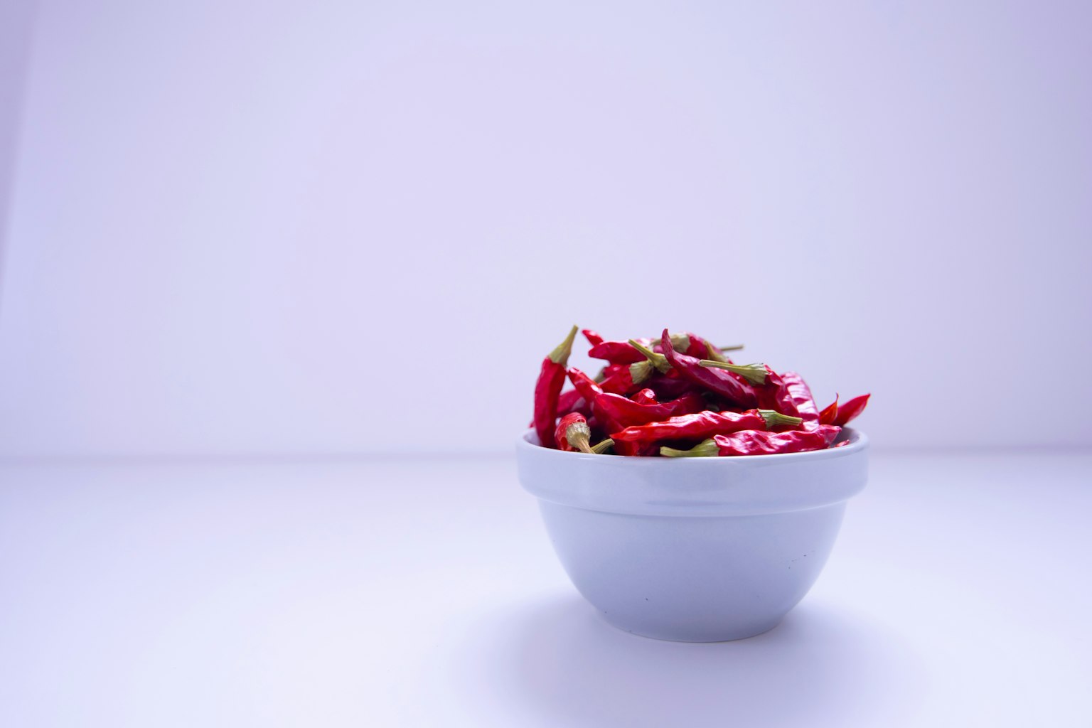 A blue bowl filled with red chili peppers against a white background
