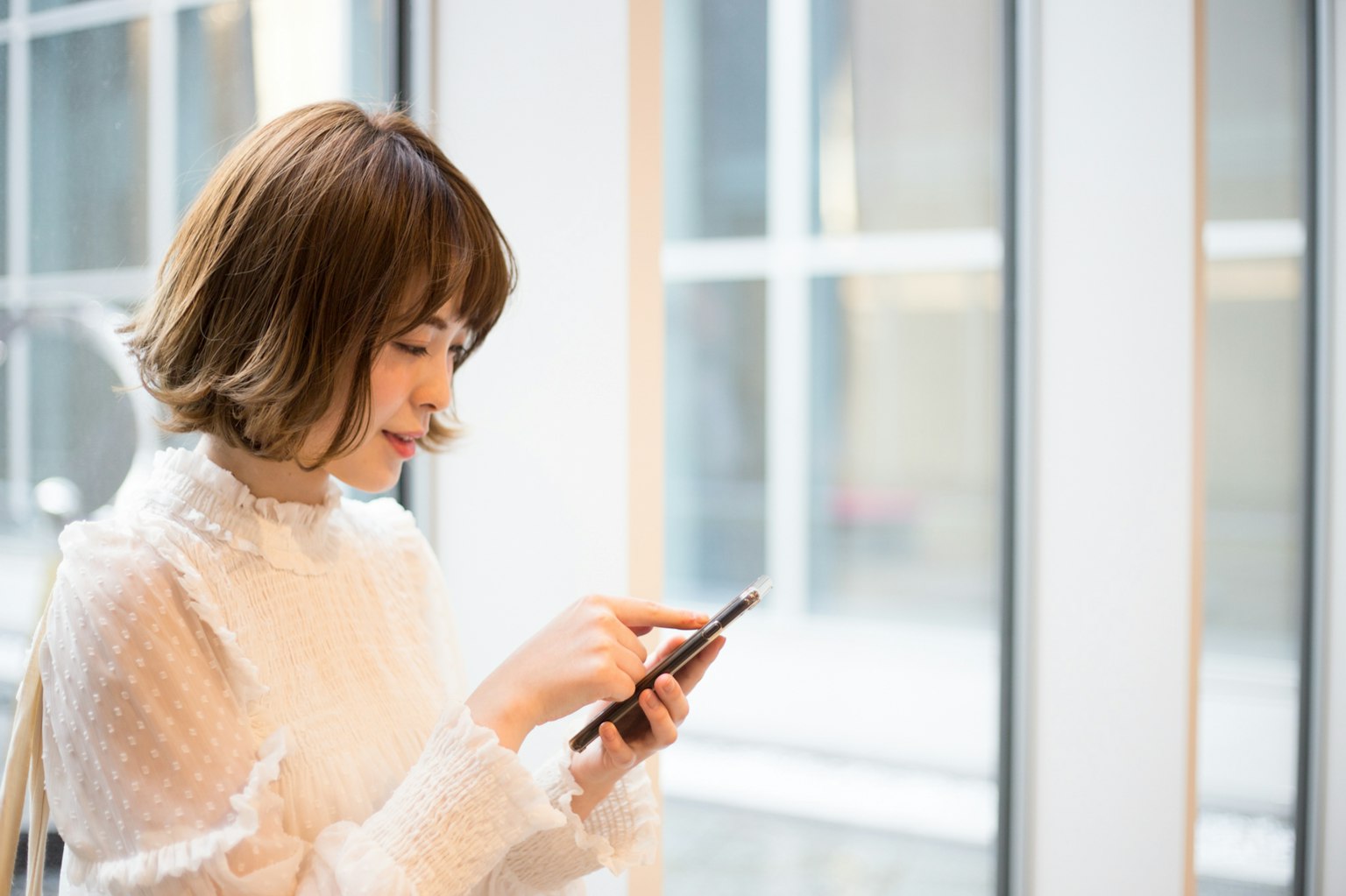 Frau, die ein Smartphone in der Nähe eines Fensters benutzt