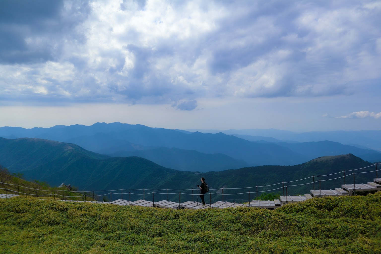 Person standing on a path with mountains and clouds in the background