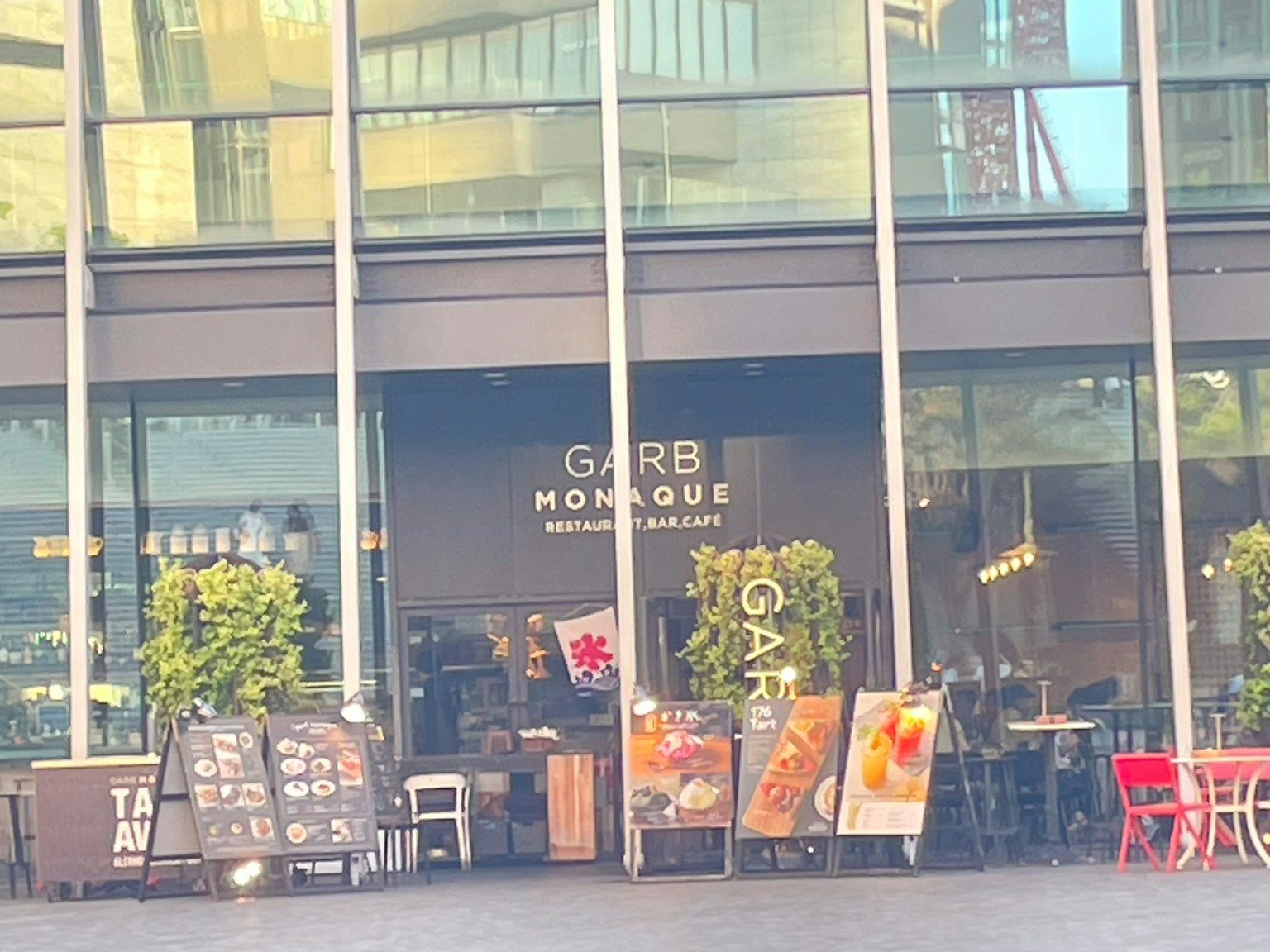 Eksterior Garb Monque dengan tanaman hijau dan papan menu