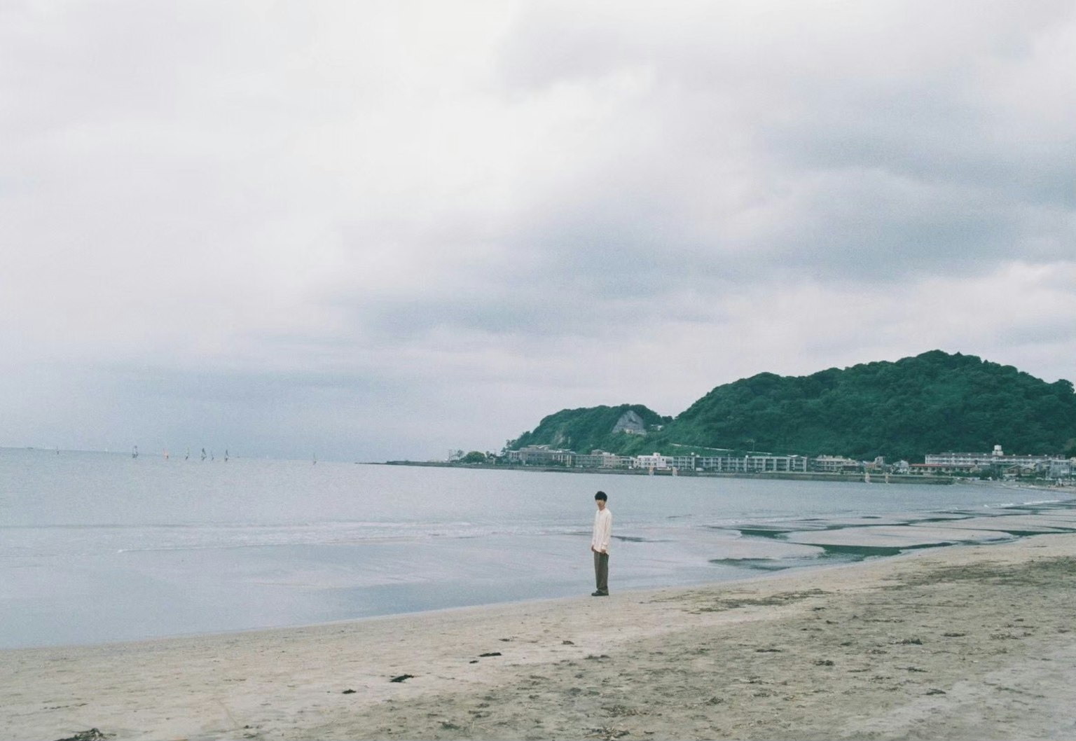 Seseorang berdiri di pantai yang tenang, menatap kejauhan