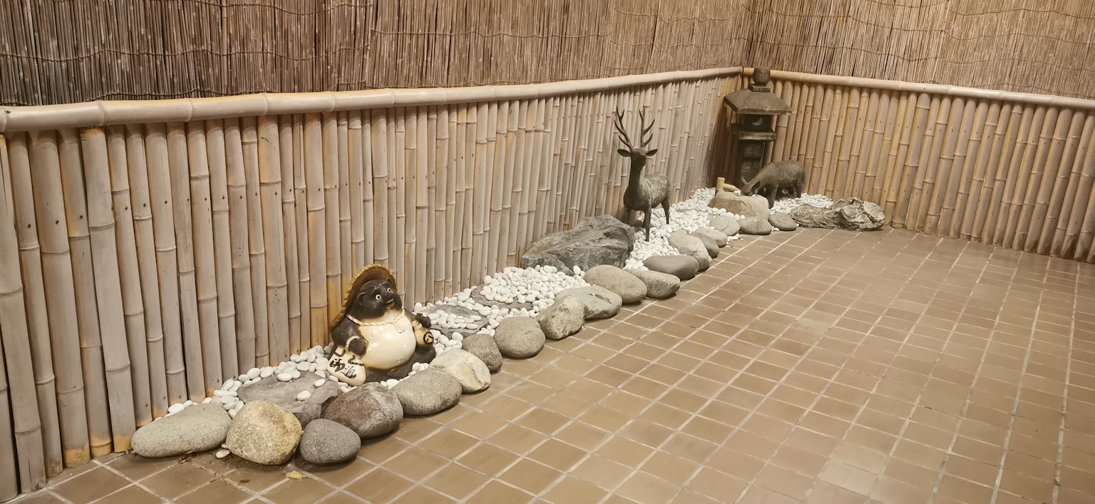 Ruang dalam dengan dinding bambu menampilkan batu dan patung rusa
