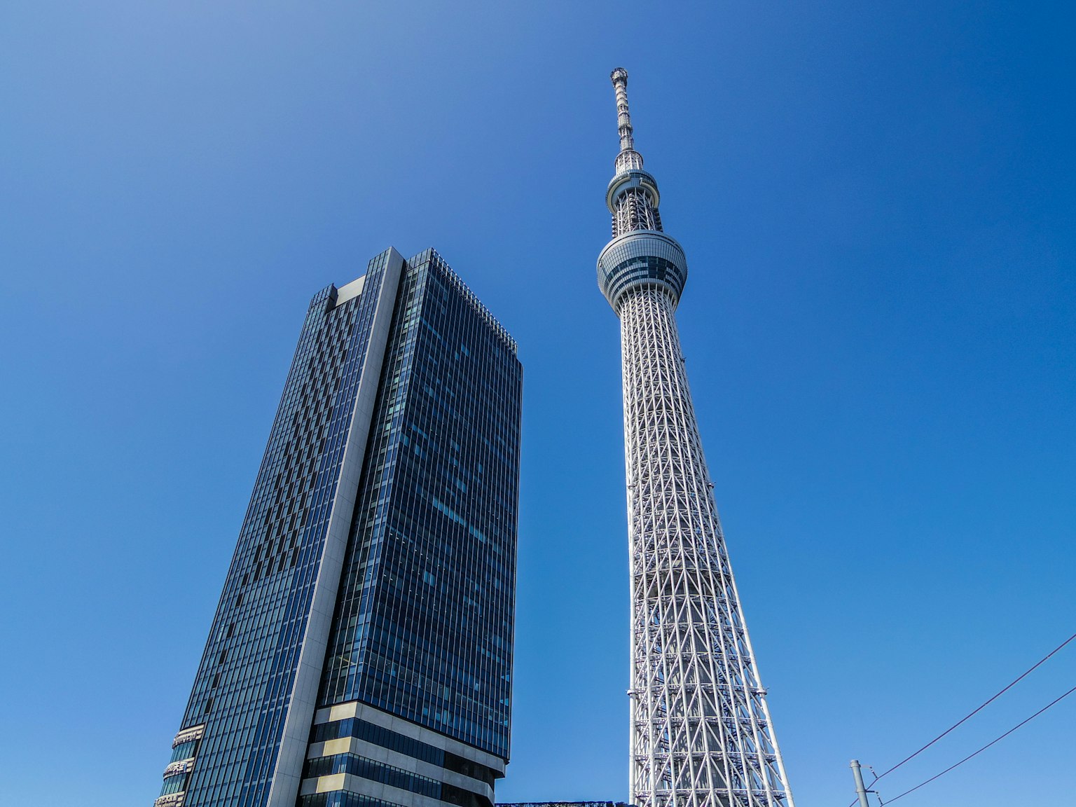 Tokyo Skytree neben einem modernen Wolkenkratzer unter einem klaren blauen Himmel