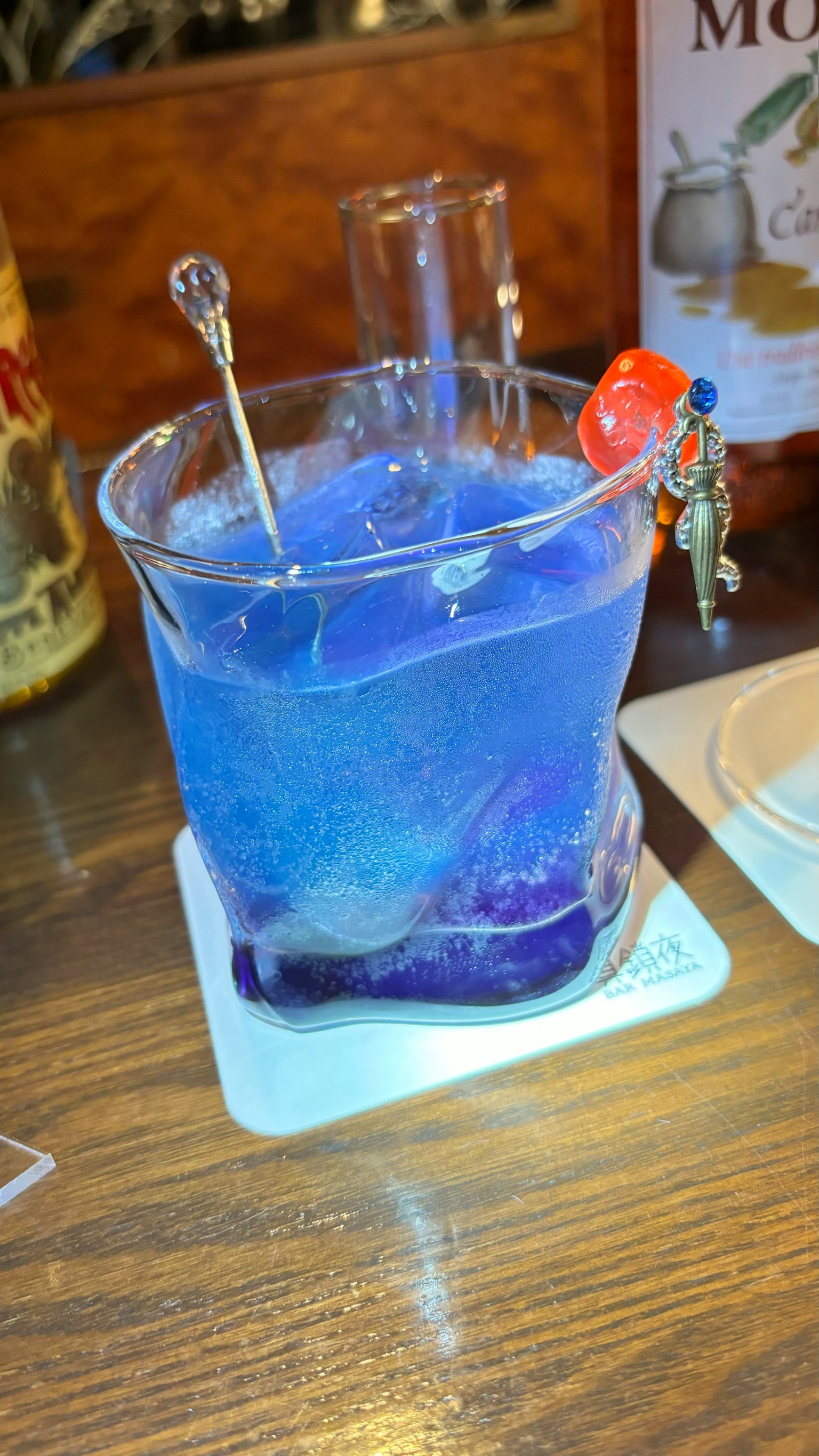 Une boisson bleue dans un verre de laboratoire avec des piques et une cerise en garniture