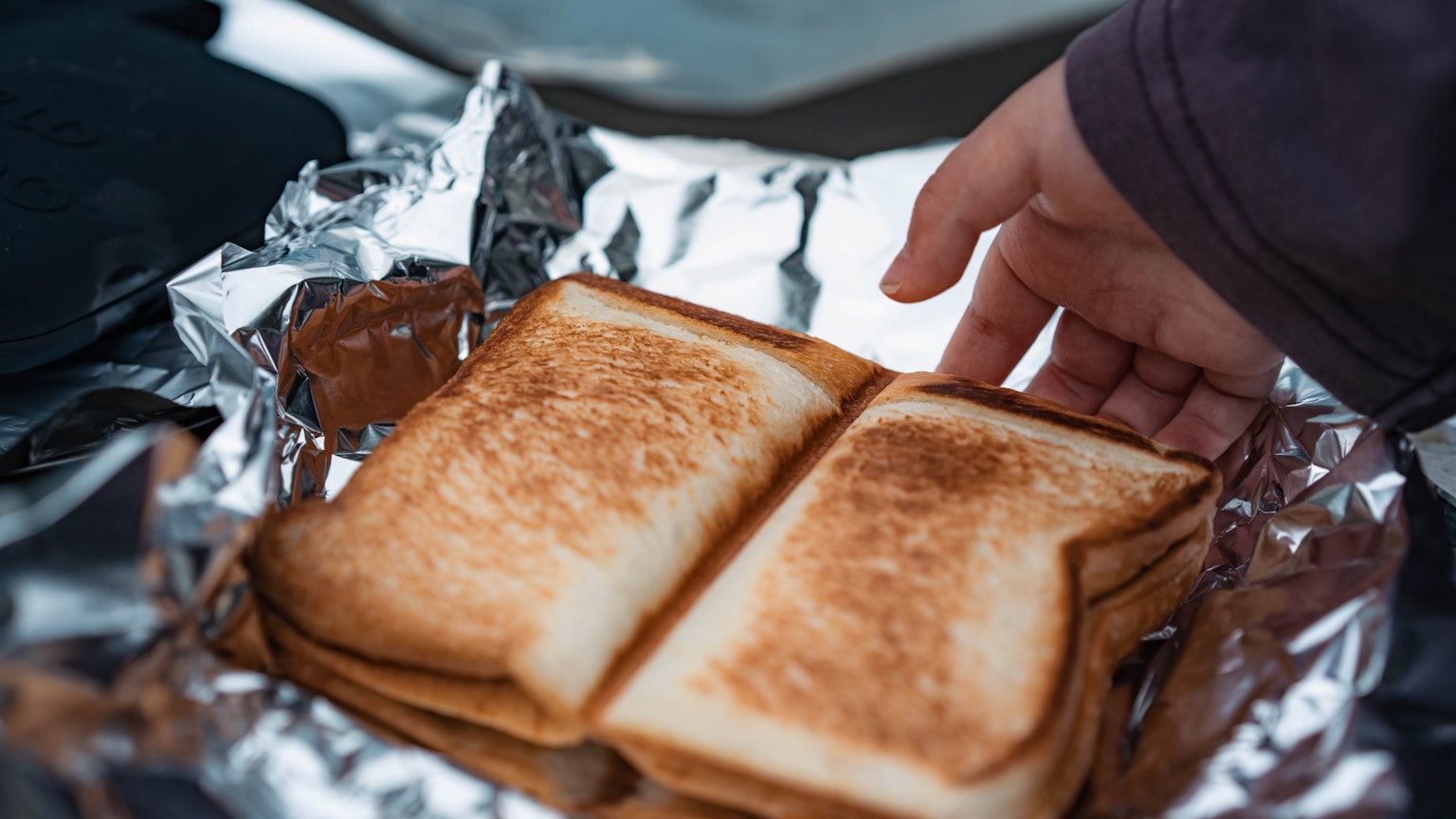Kedekatan roti panggang di atas aluminium foil dengan tangan yang mendekat