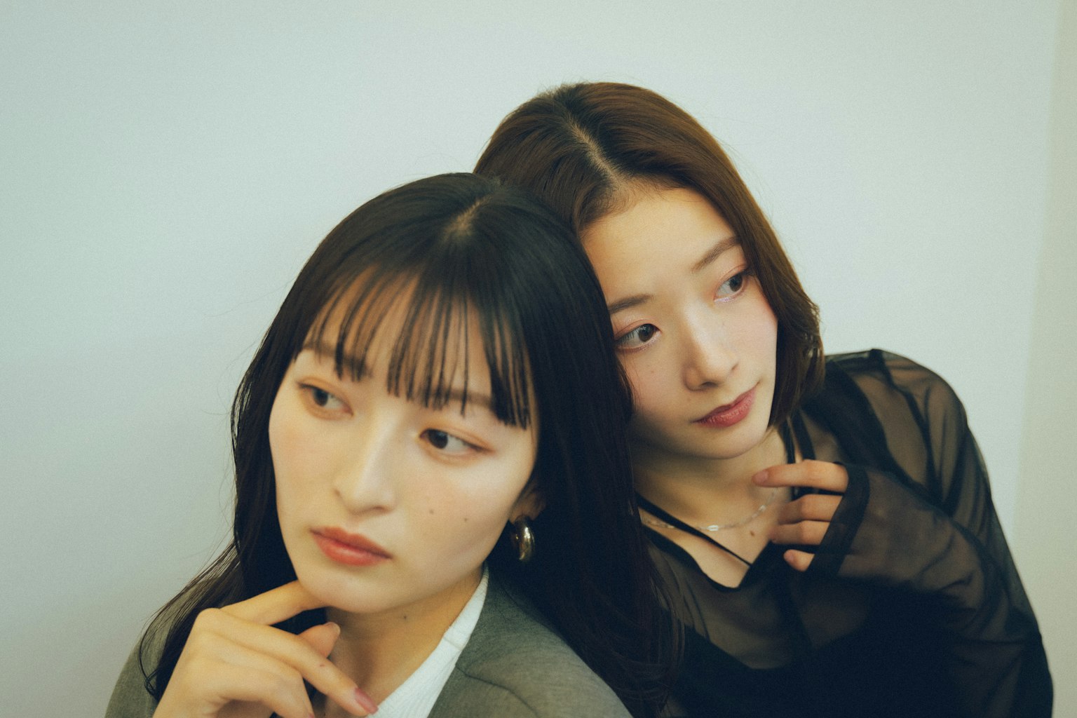 Potret dua wanita bersandar satu sama lain Satu memiliki rambut hitam dengan poni Yang lain memiliki rambut panjang dan ekspresi halus