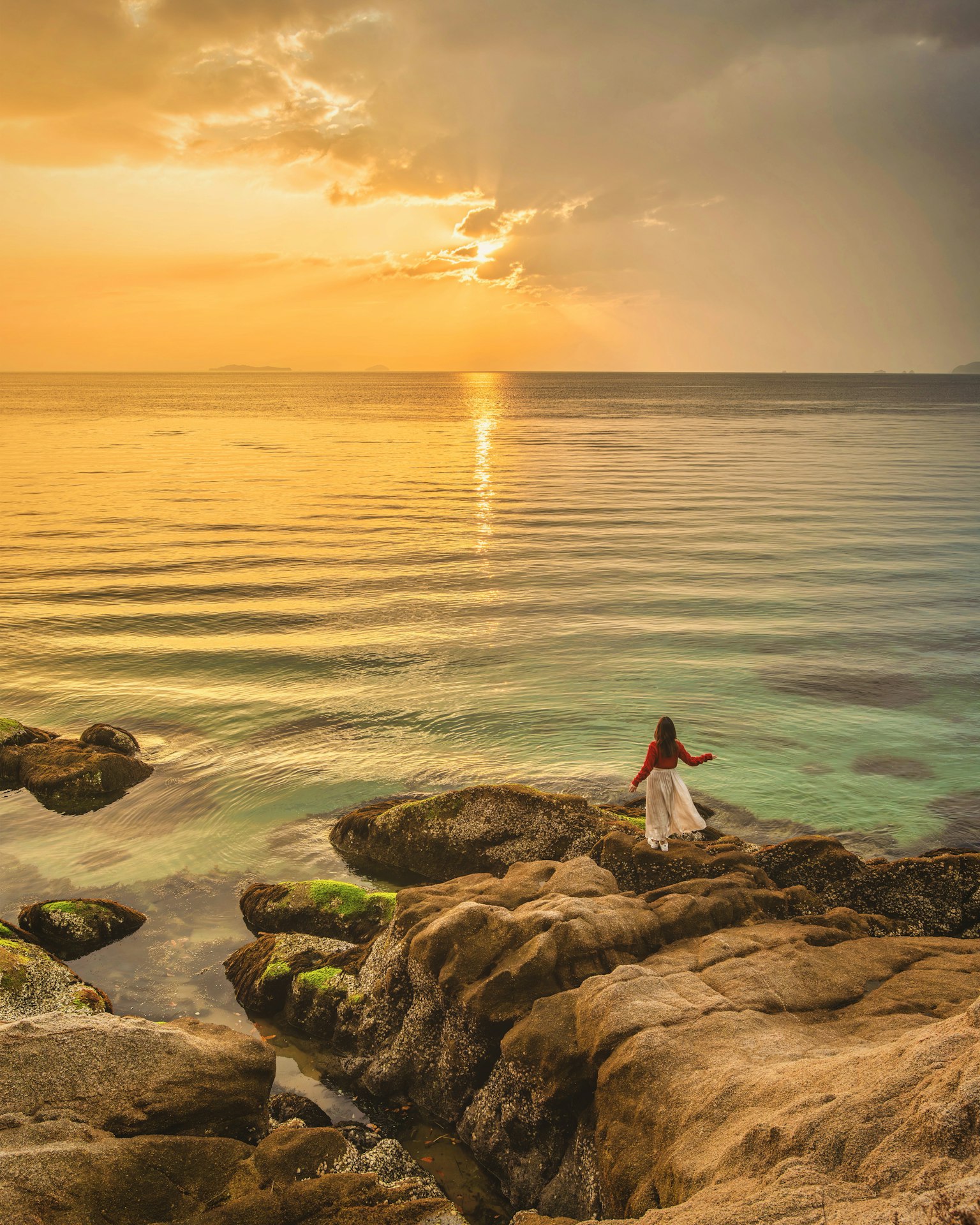 Una mujer de pie sobre rocas junto al mar durante un hermoso atardecer