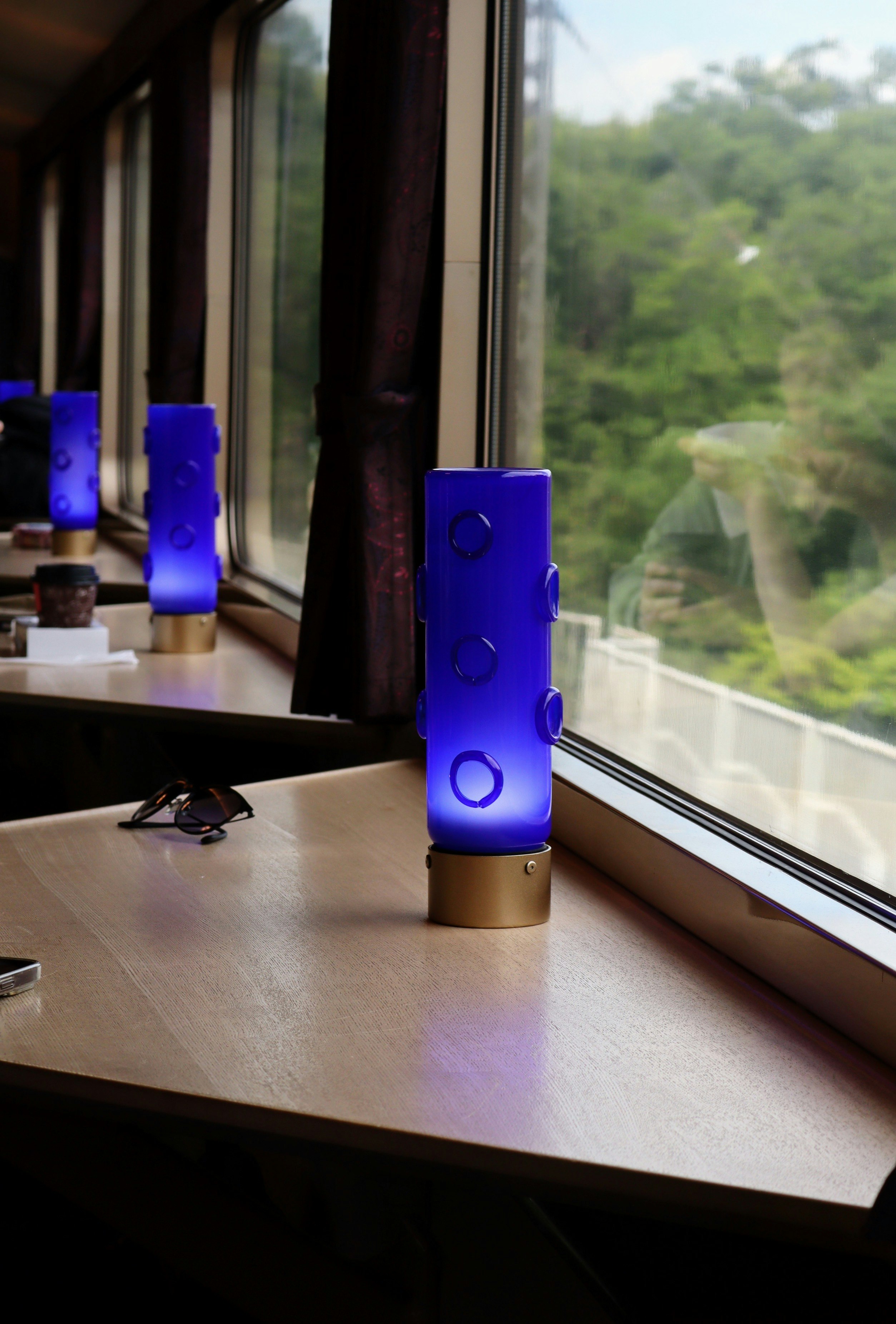 窓辺のテーブルに置かれた青い電車旅グッズと車窓の景色