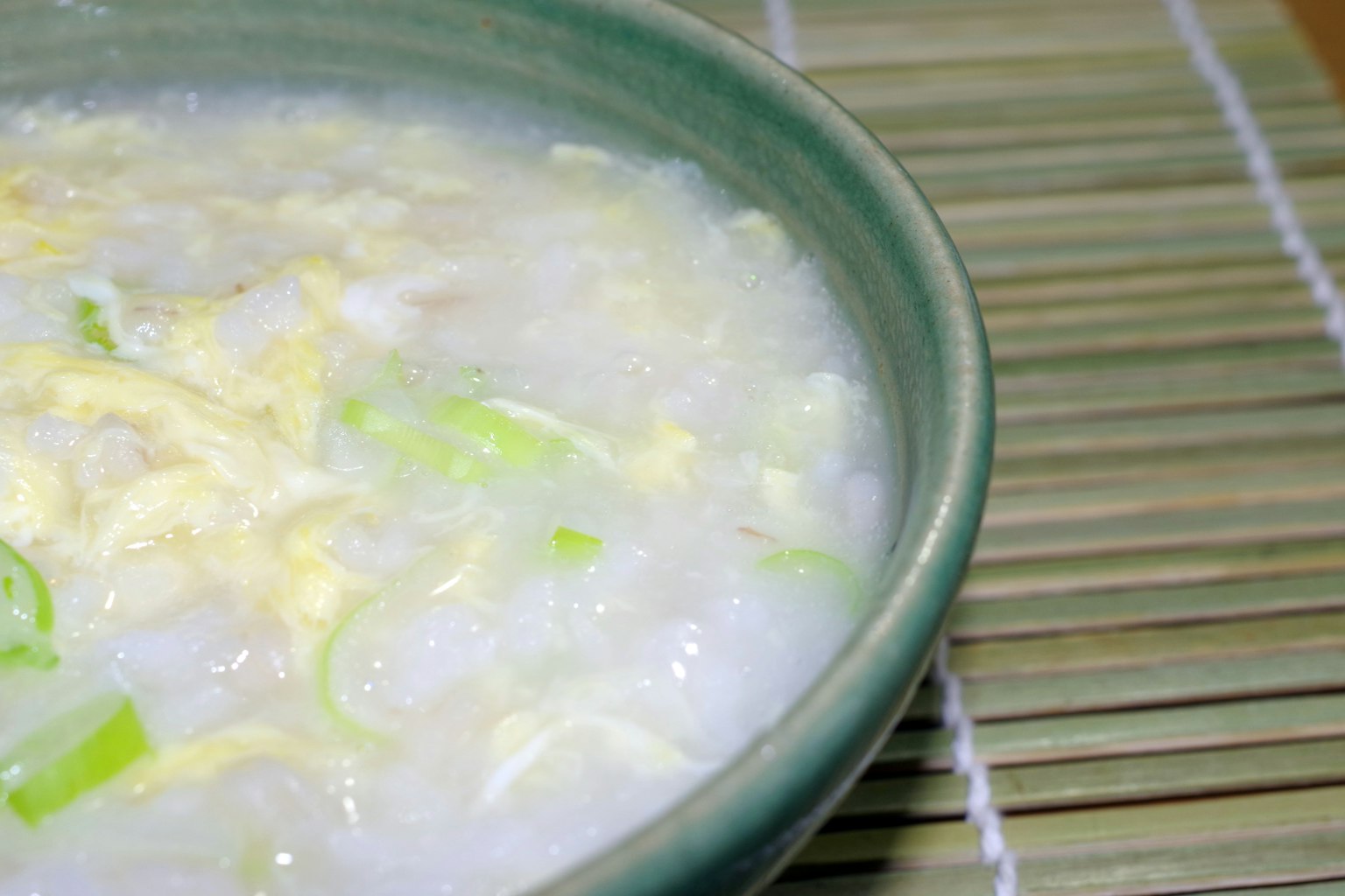 Primo piano di congee in una ciotola verde guarnito con cipollotti tritati e uova