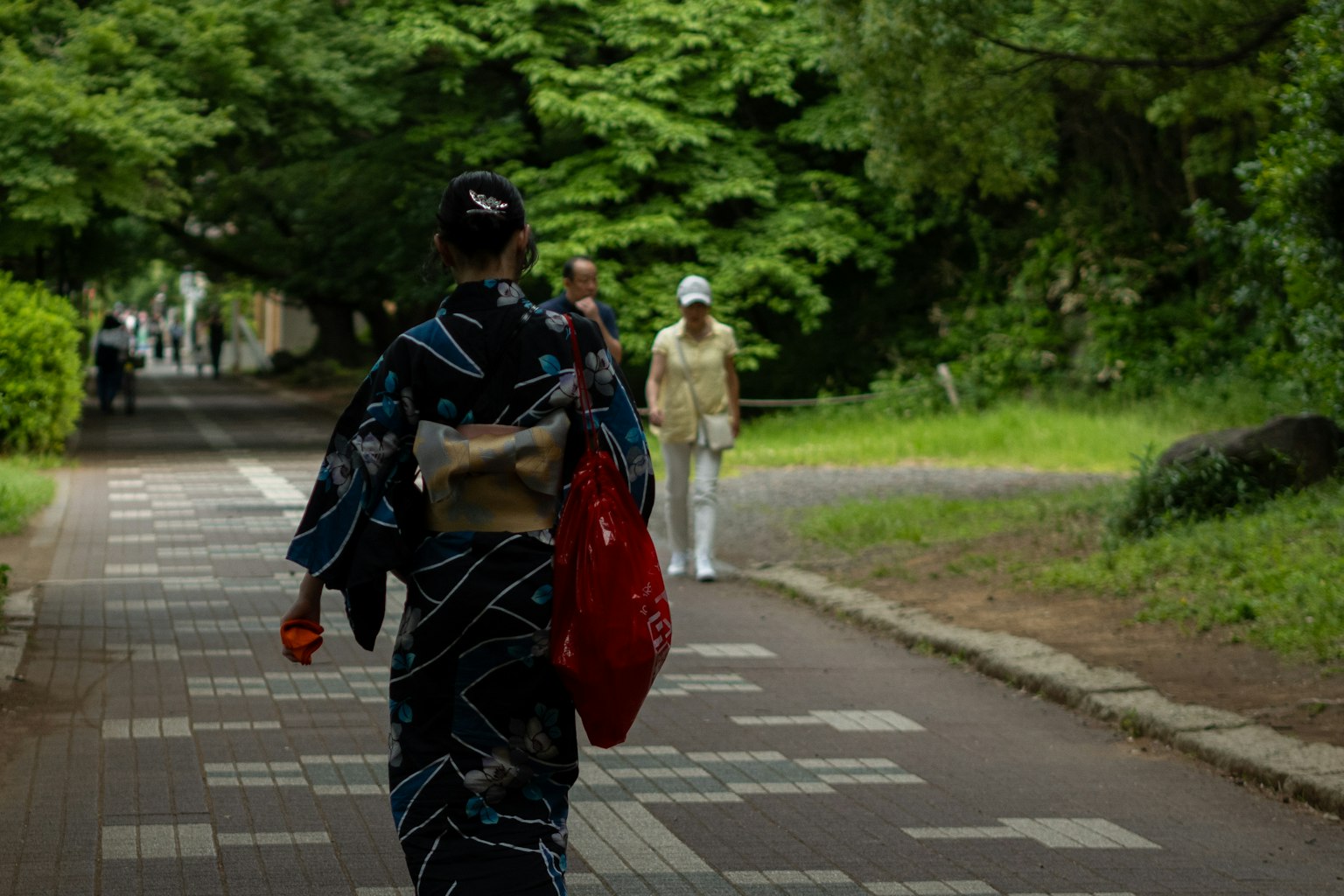 Eine Frau im Kimono läuft einen Weg entlang, umgeben von üppigem Grün