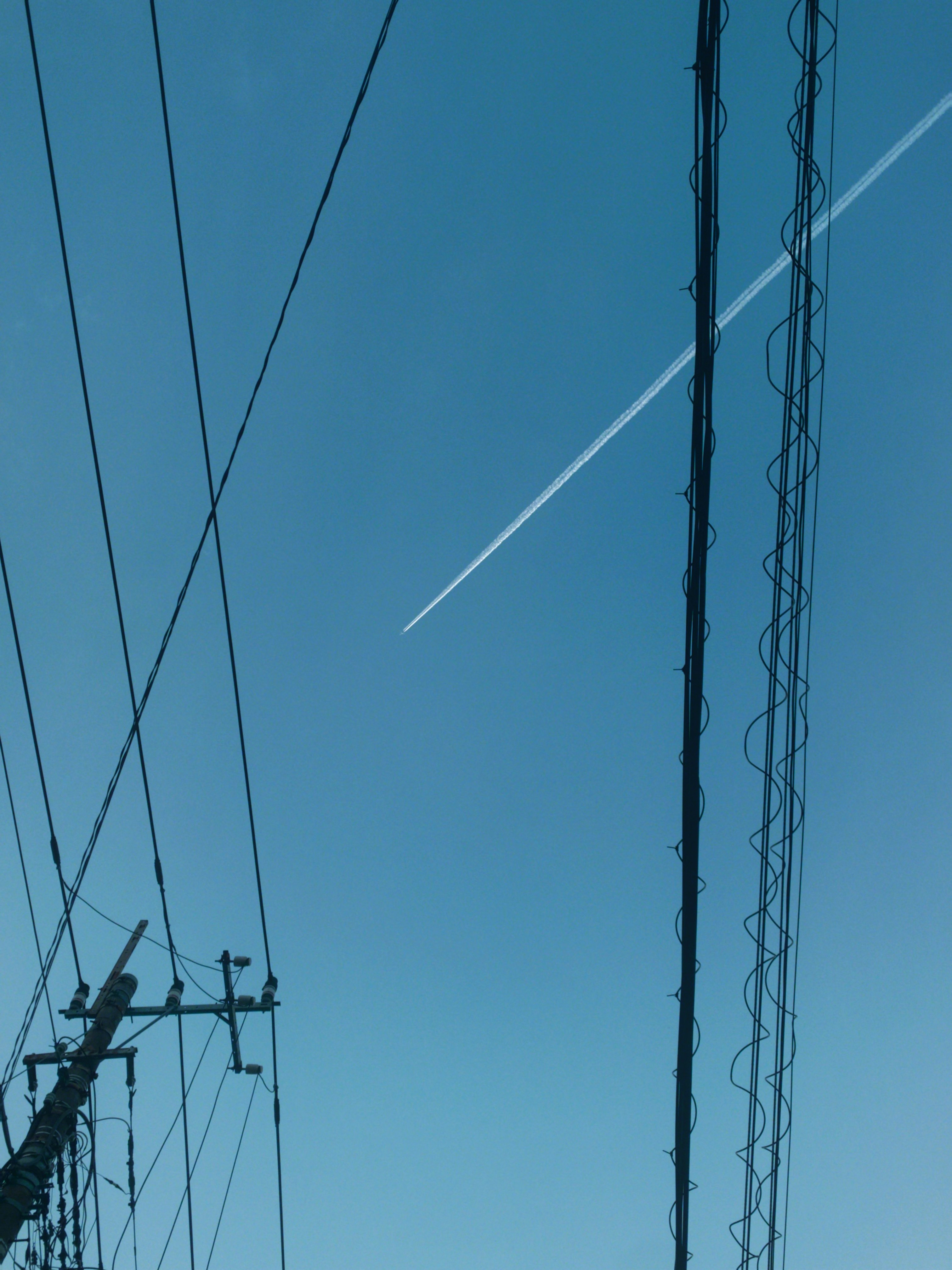 青空に伸びる電線と送電鉄塔のシルエット