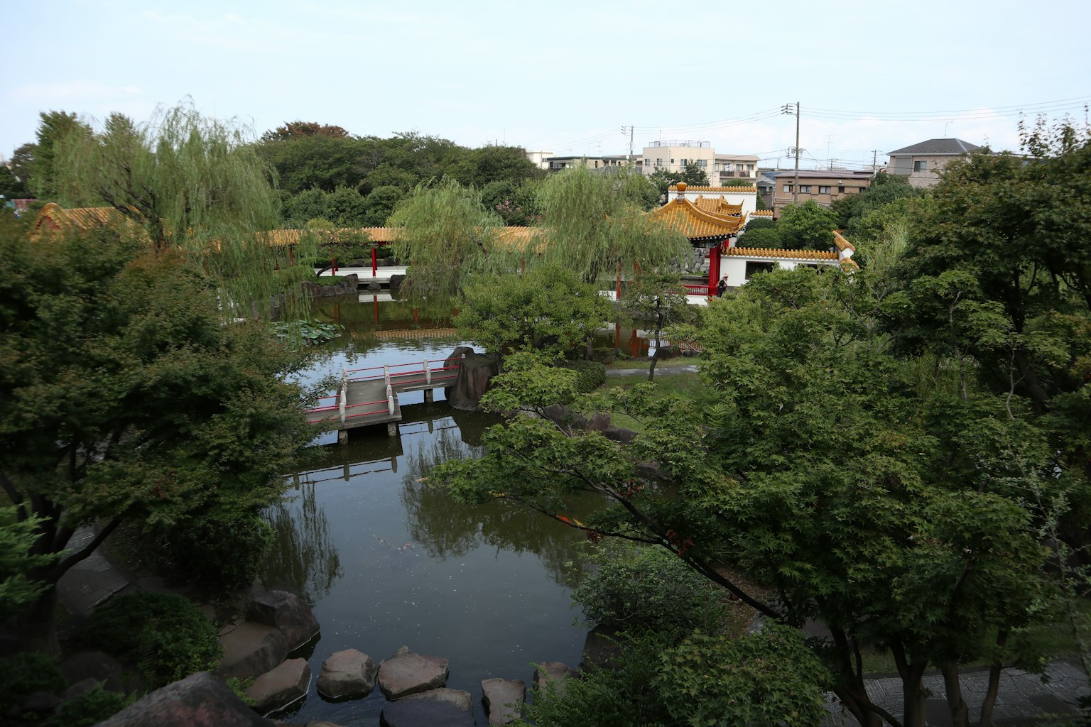 ทิวทัศน์สวนญี่ปุ่นที่มีบ่อและสะพานพืชพรรณเขียวขจีและน้ำสงบ