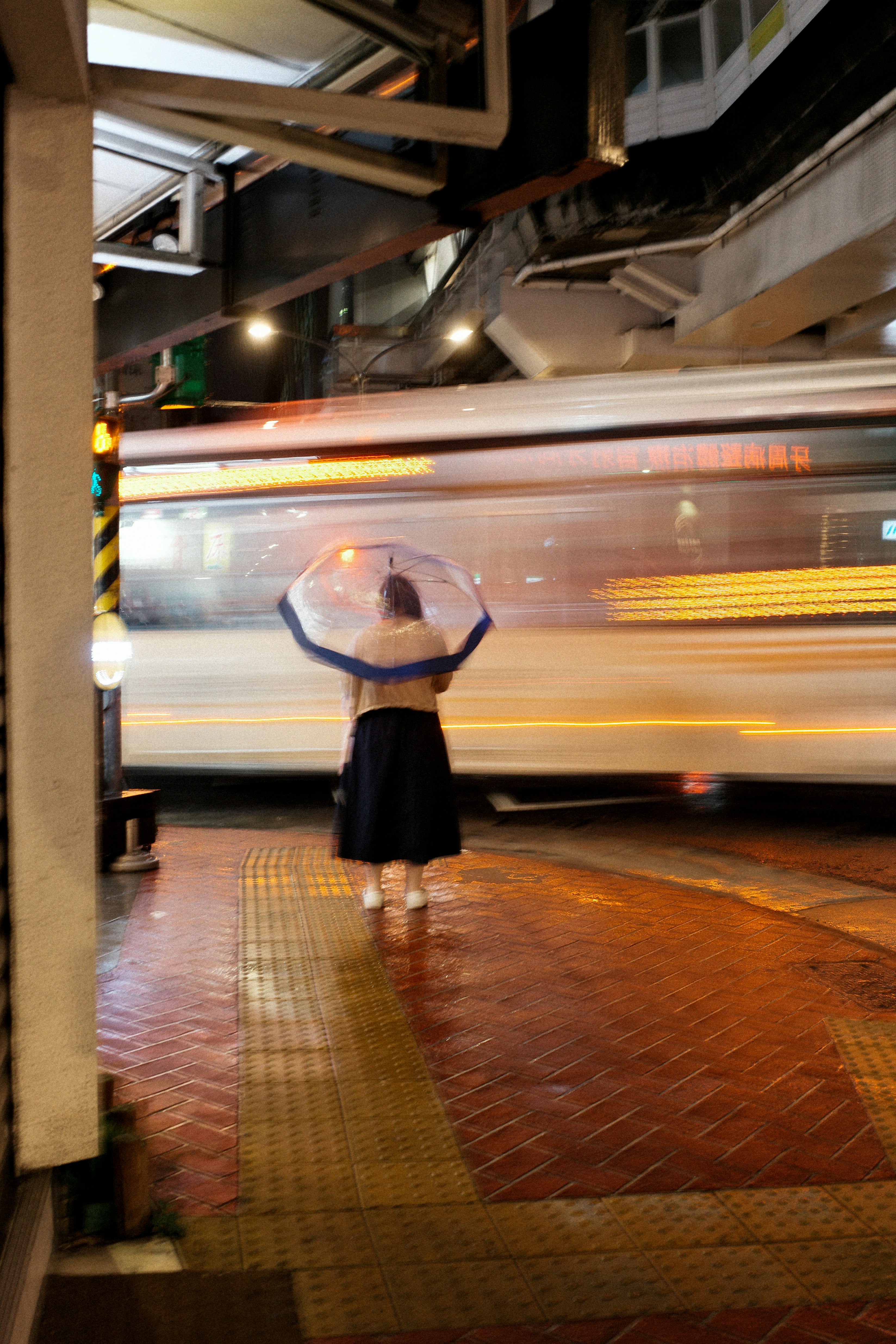高架下で手を振る人物と走り去る電車の光跡