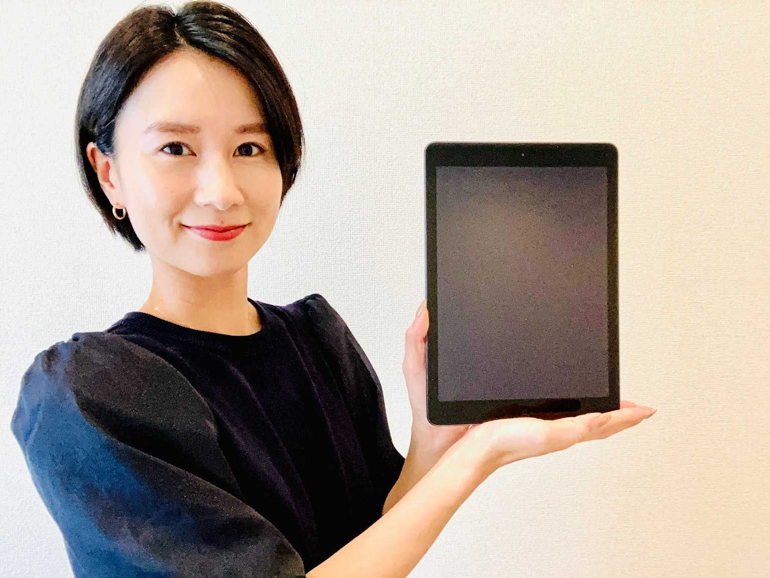 Una donna che sorride mentre tiene un tablet su uno sfondo semplice