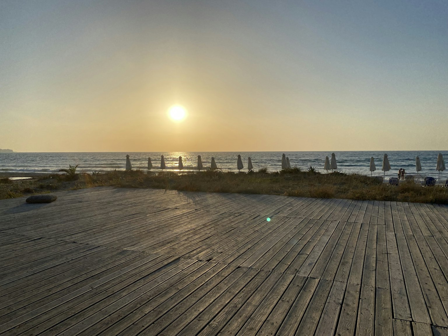 ฉากชายหาดกับพระอาทิตย์ตกเหนือมหาสมุทรระเบียงไม้และร่มชายหาด